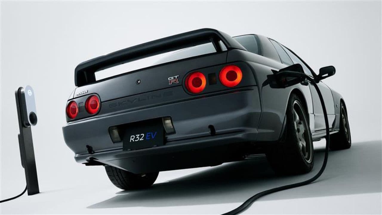 Rear view of the Nissan Skyline R32 GT-R EV, plugged into a charging station, showcasing its classic tail lights and modern R32 EV badge.