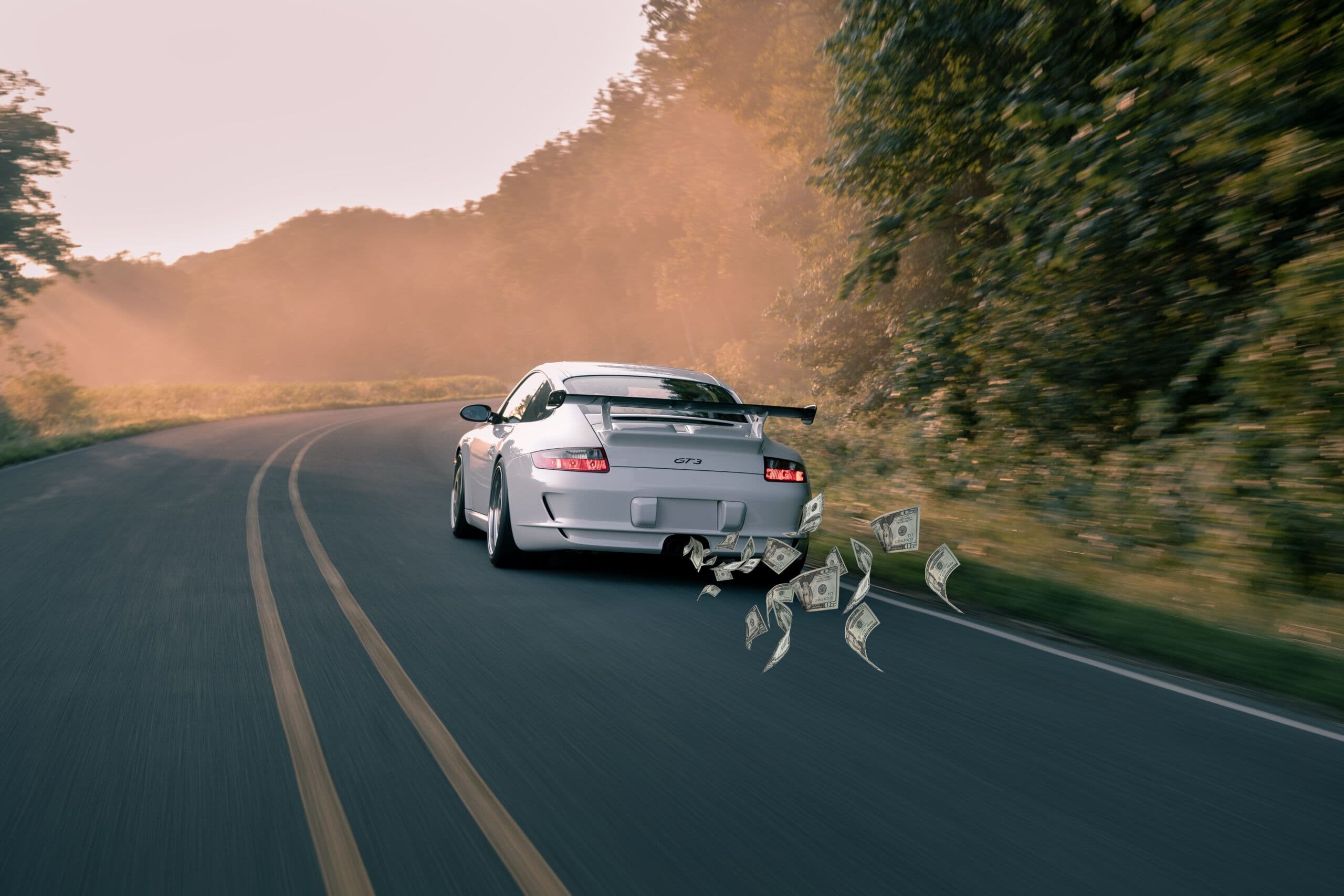 Porsche 911 GT3 driving on country road with dollar bills trailing behind, representing high running costs
