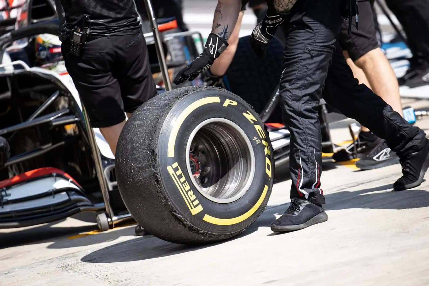 A heavily worn Pirelli P Zero medium compound Formula 1 tyre being removed in the pit lane, yellow sidewall lettering visible with significant rubber degradation across the tread surface