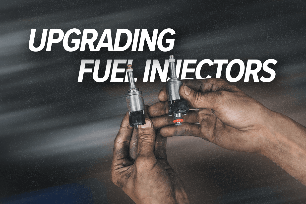Close-up of two fuel injectors being compared during an upgrade, showing old vs new parts for a performance engine build.