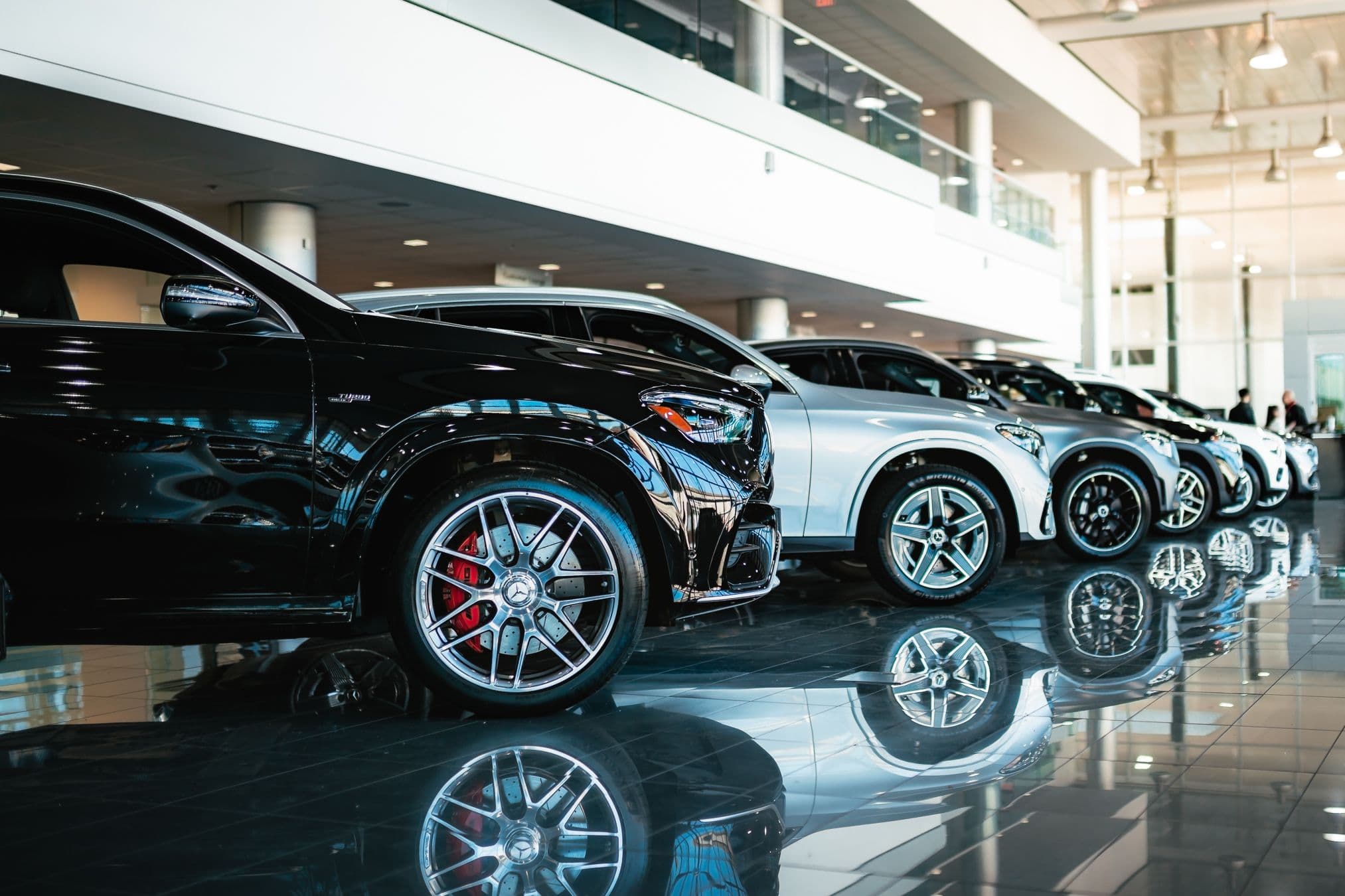 Row of Mercedes-Benz SUVs including AMG models inside a modern showroom, reflecting on polished tile flooring.