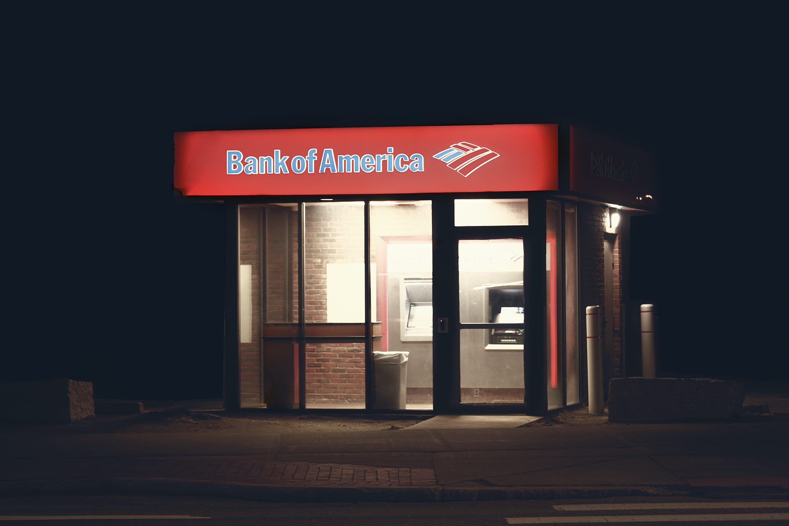 Bank of America ATM branch at night with red signage and dimly lit interior visible through glass