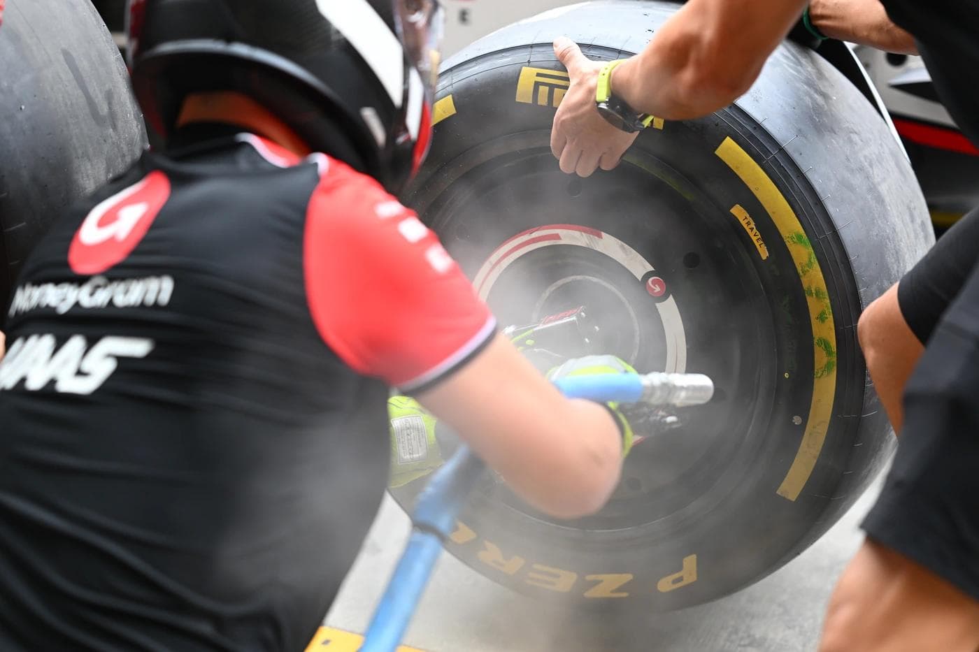 Haas F1 mechanic using a wheel gun to secure a Pirelli P Zero tyre during pit stop practice at Yas Marina Circuit, yellow medium compound sidewall marking visible with brake disc heat haze in the background