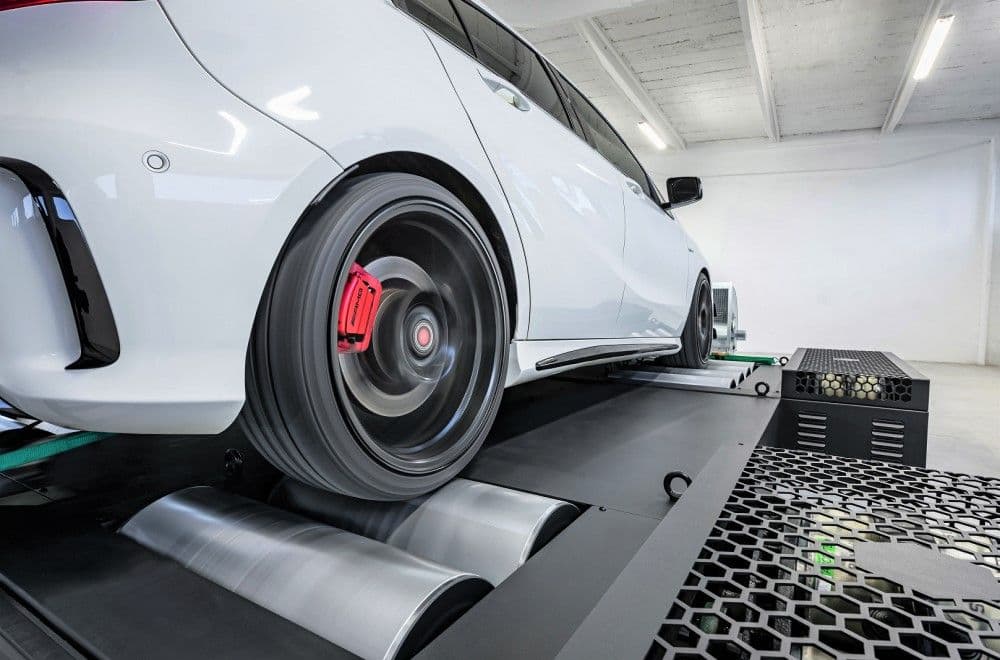 White Mercedes-Benz A45 AMG undergoing dyno tuning test, showing rear wheel on rolling road during power measurement session in a clean workshop.