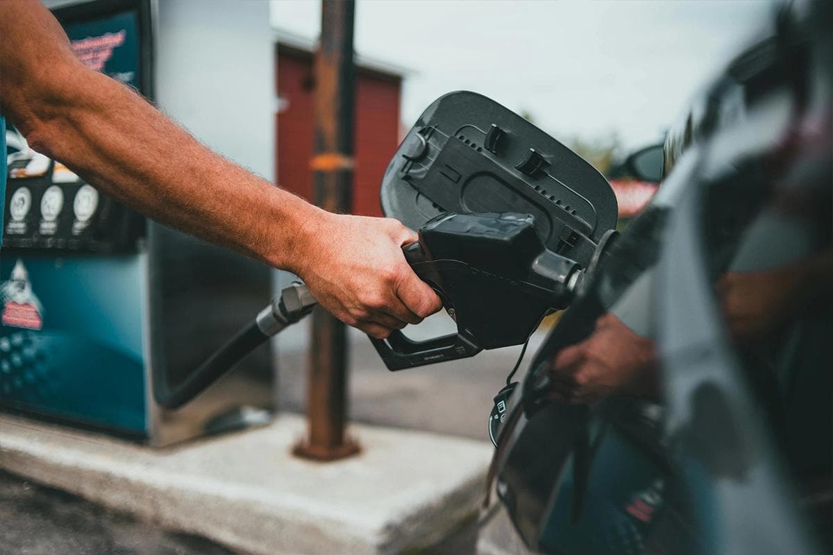 Closeup of a driver refuelling a car at a petrol station with a fuel nozzle inserted into the filler neck.