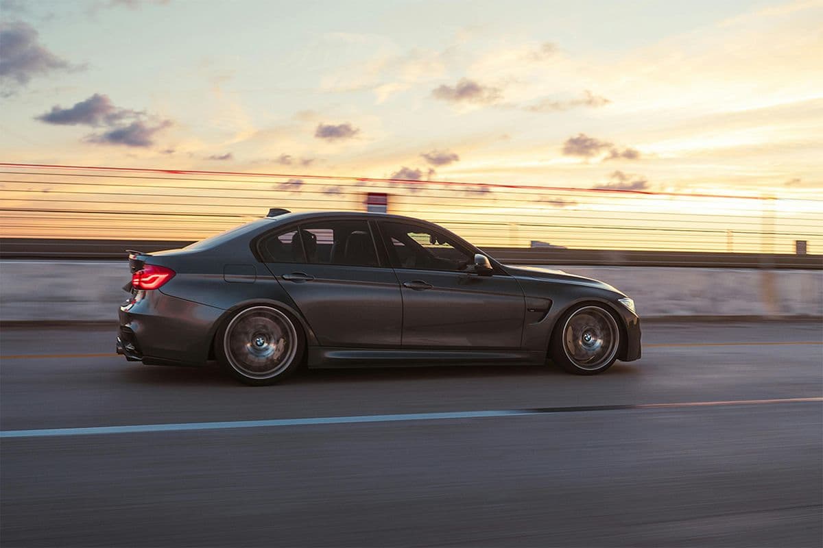 BMW F80 M3 driving at speed on an open road during sunset.