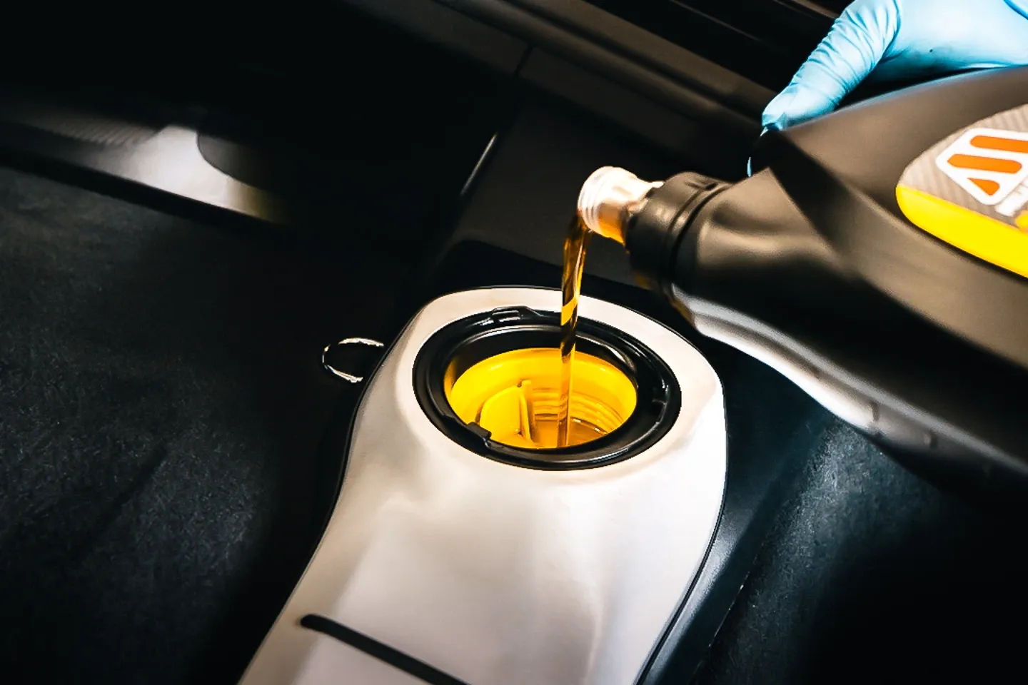 Engine oil being poured into the oil filler cap of a Porsche Cayman GTS during a routine maintenance service.
