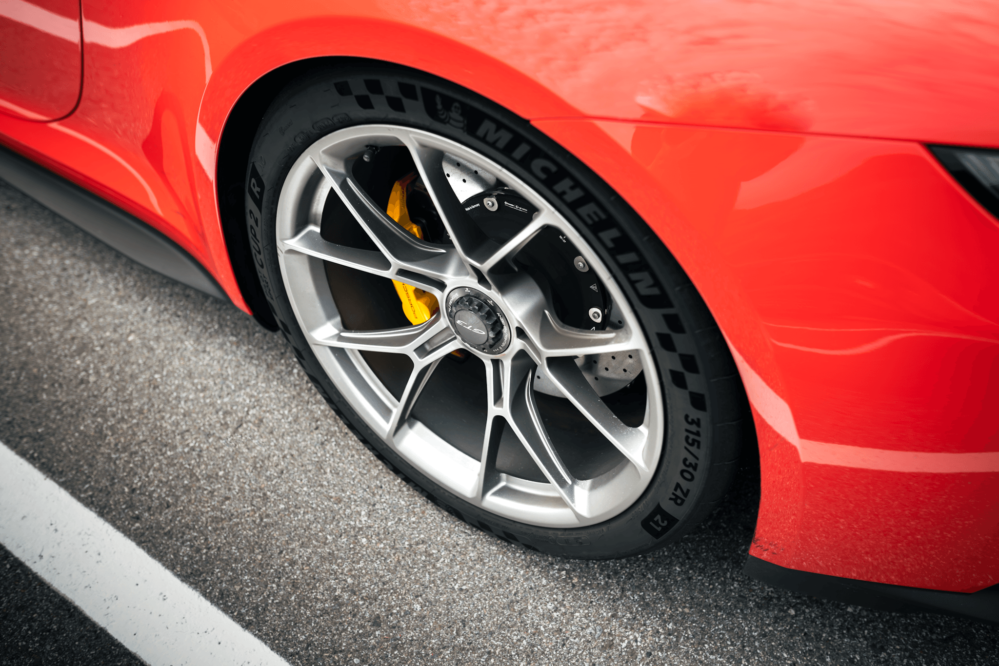 Close-up of a Michelin Pilot Sport Cup 2 tyre and alloy wheel on a red high-performance sports car, highlighting the 315/30 ZR size and carbon-ceramic brakes.