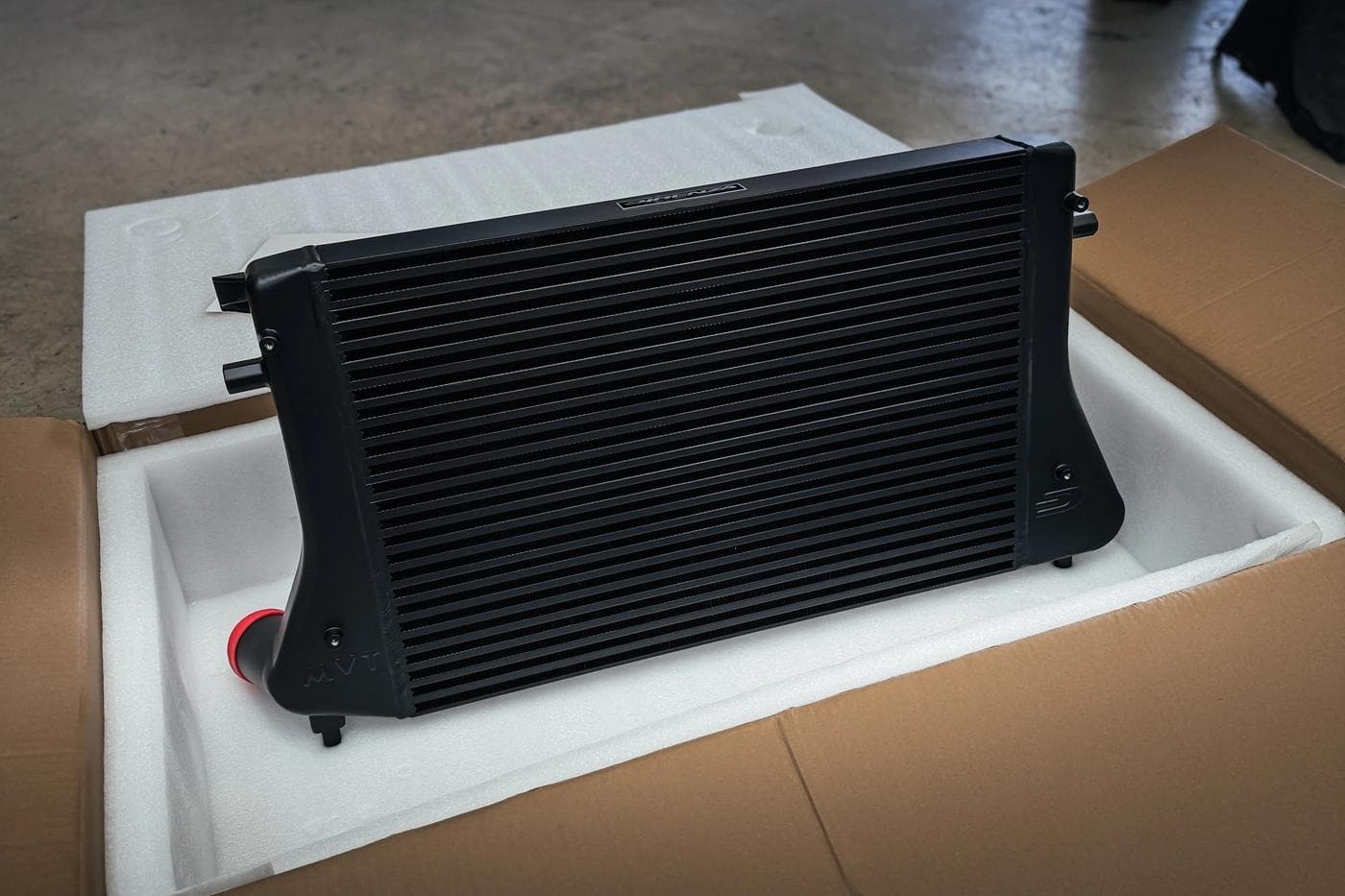 Direnza MVT intercooler in packaging, showing TIG welded construction and black anodised finish ready for installation.