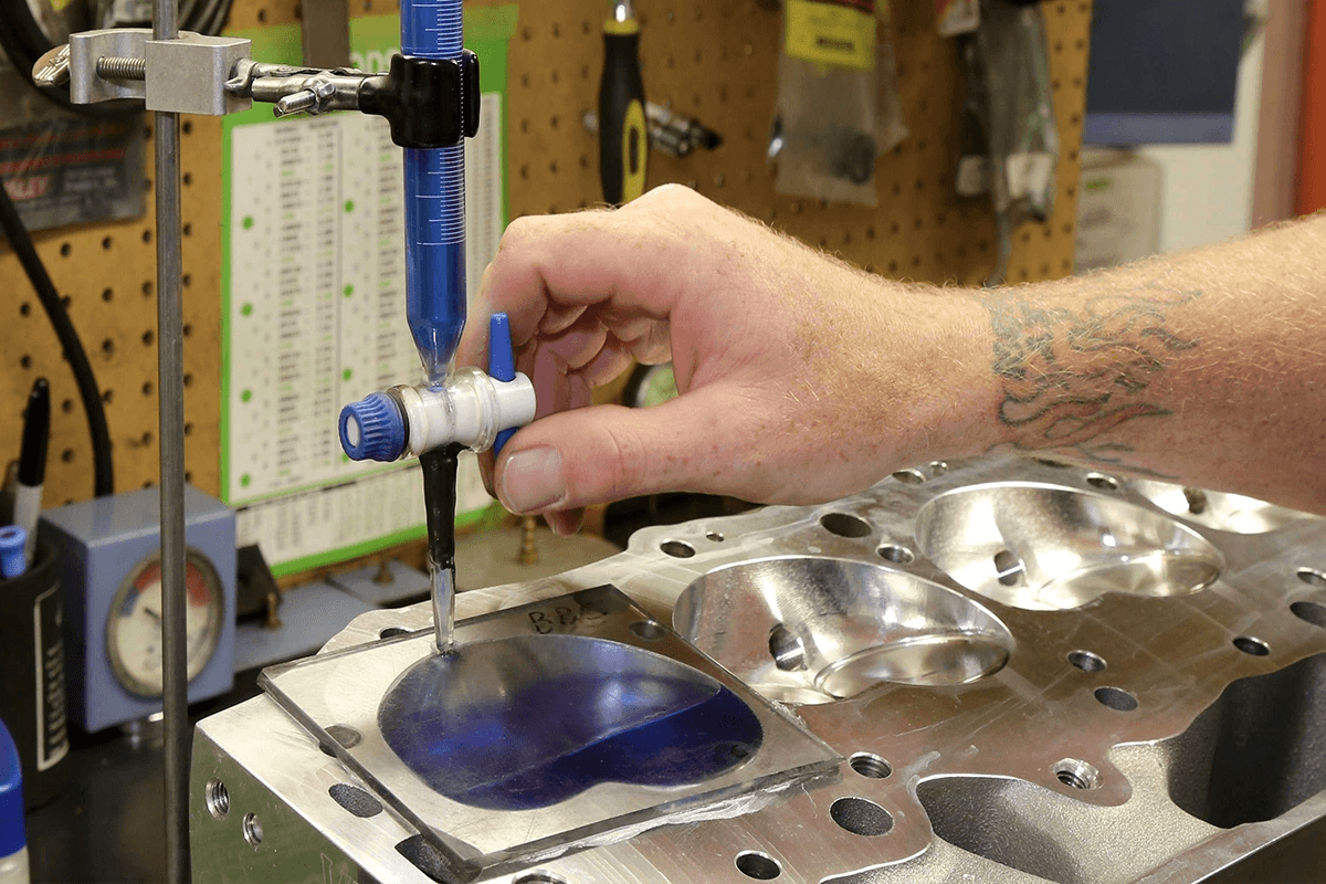 Technician measuring combustion chamber volume with a burette and plate to calculate engine compression ratio.