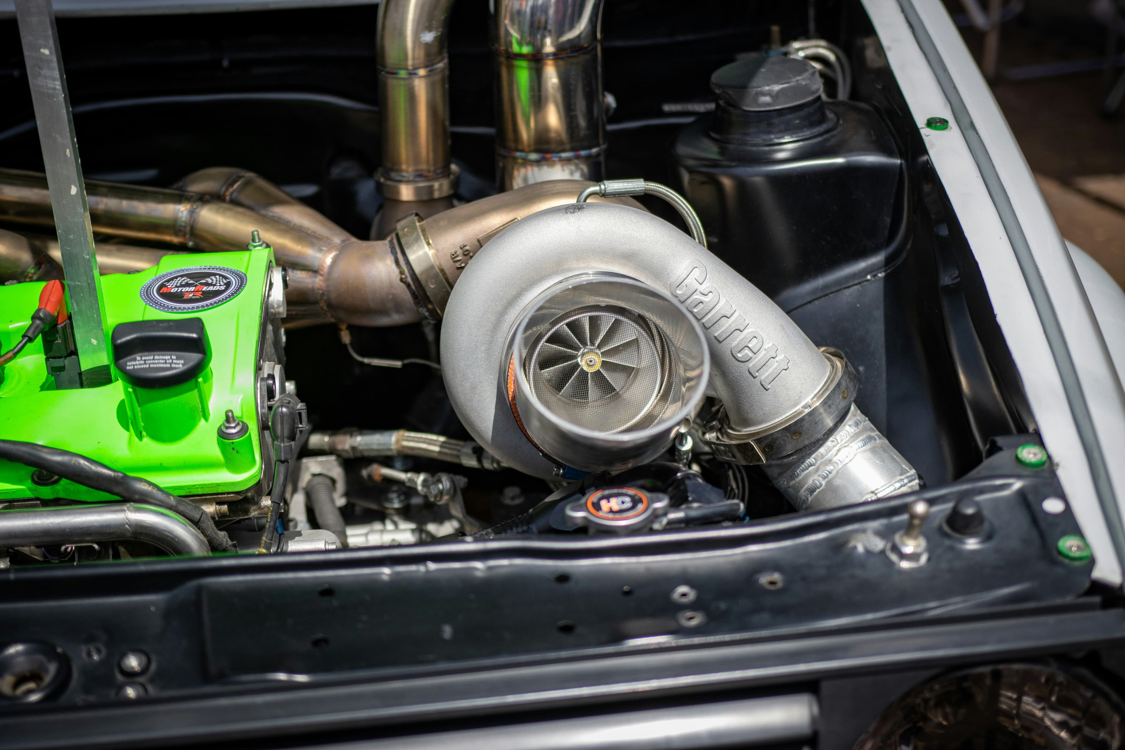 Close-up of a Garrett turbocharger installed in a modified engine bay, highlighting aftermarket exhaust fabrication and forced induction upgrades for improved volumetric efficiency.