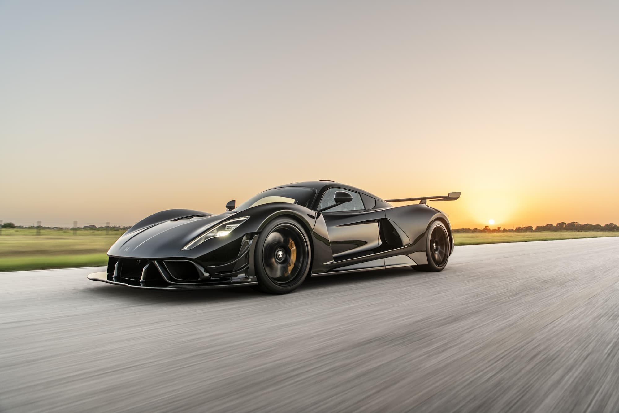Black Hennessey Venom F5 hypercar with extended rear wing driving at dusk, engineered for extreme top speed.
