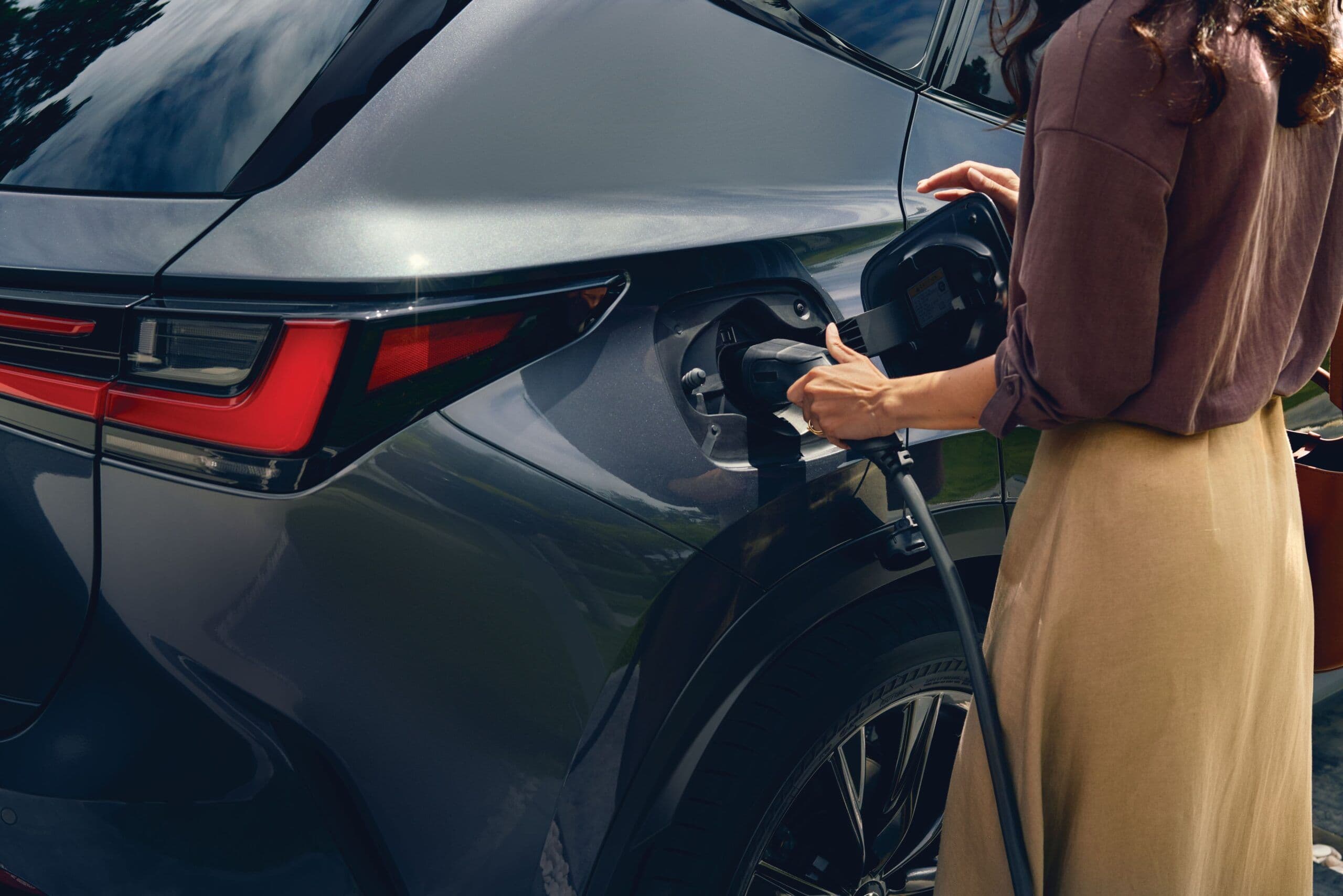 Woman charging a silver electric SUV at home, illustrating eco-friendly vehicle usage and EV ownership lifestyle