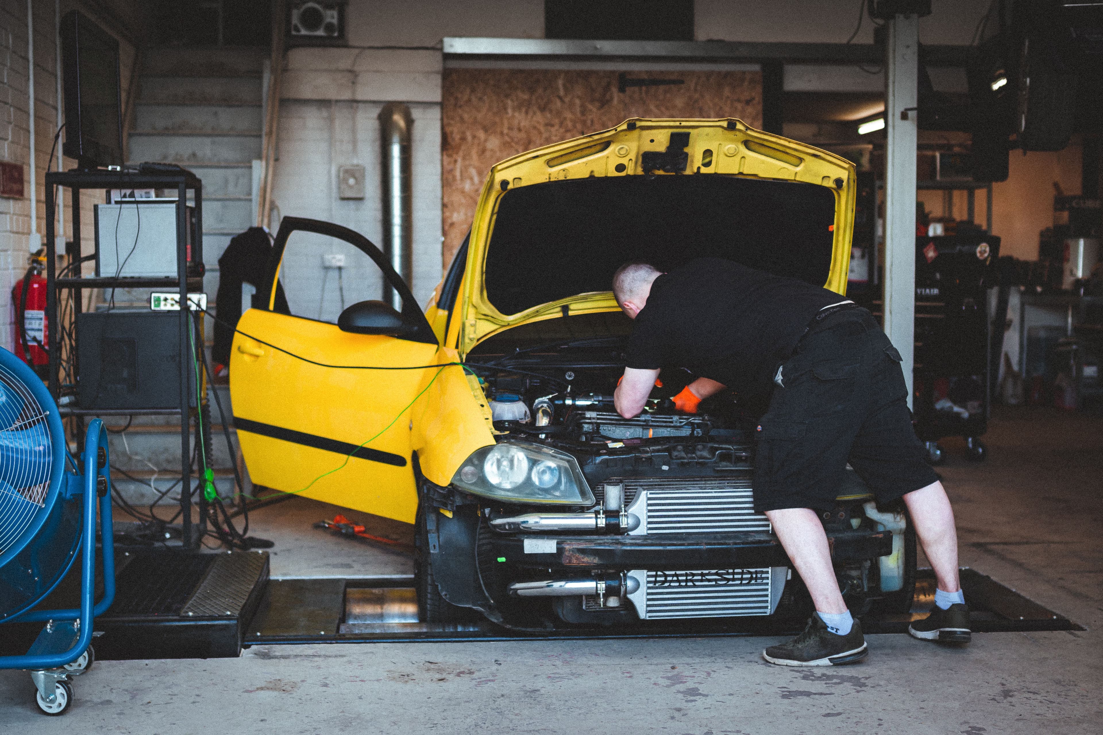 A yellow SEAT Ibiza Cupra on a dyno at JBM Performance, with the front bumper removed and a large front-mount intercooler exposed, while a mechanic leans into the engine bay for tuning work.