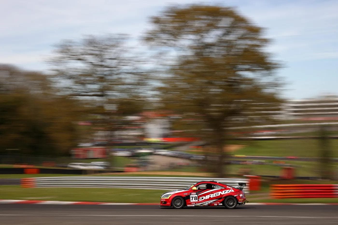 Red Direnza-branded race car on circuit demonstrating motorsport-grade thermal performance testing, showcasing engineering validation through competitive driving.