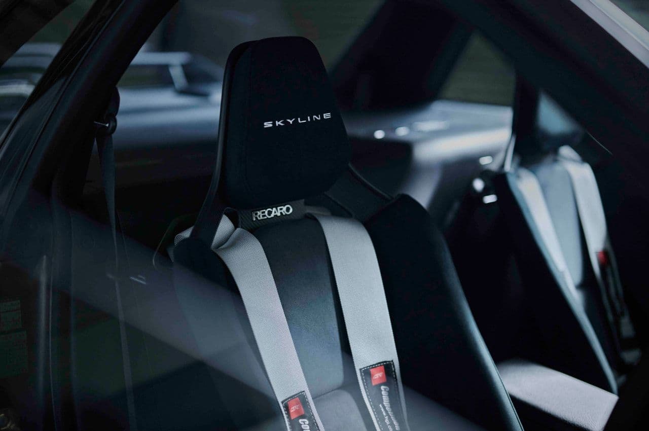 Interior view of the Nissan Skyline R32 GT-R EV featuring Recaro racing seats with harnesses, embroidered with the Skyline logo, emphasizing performance and comfort.