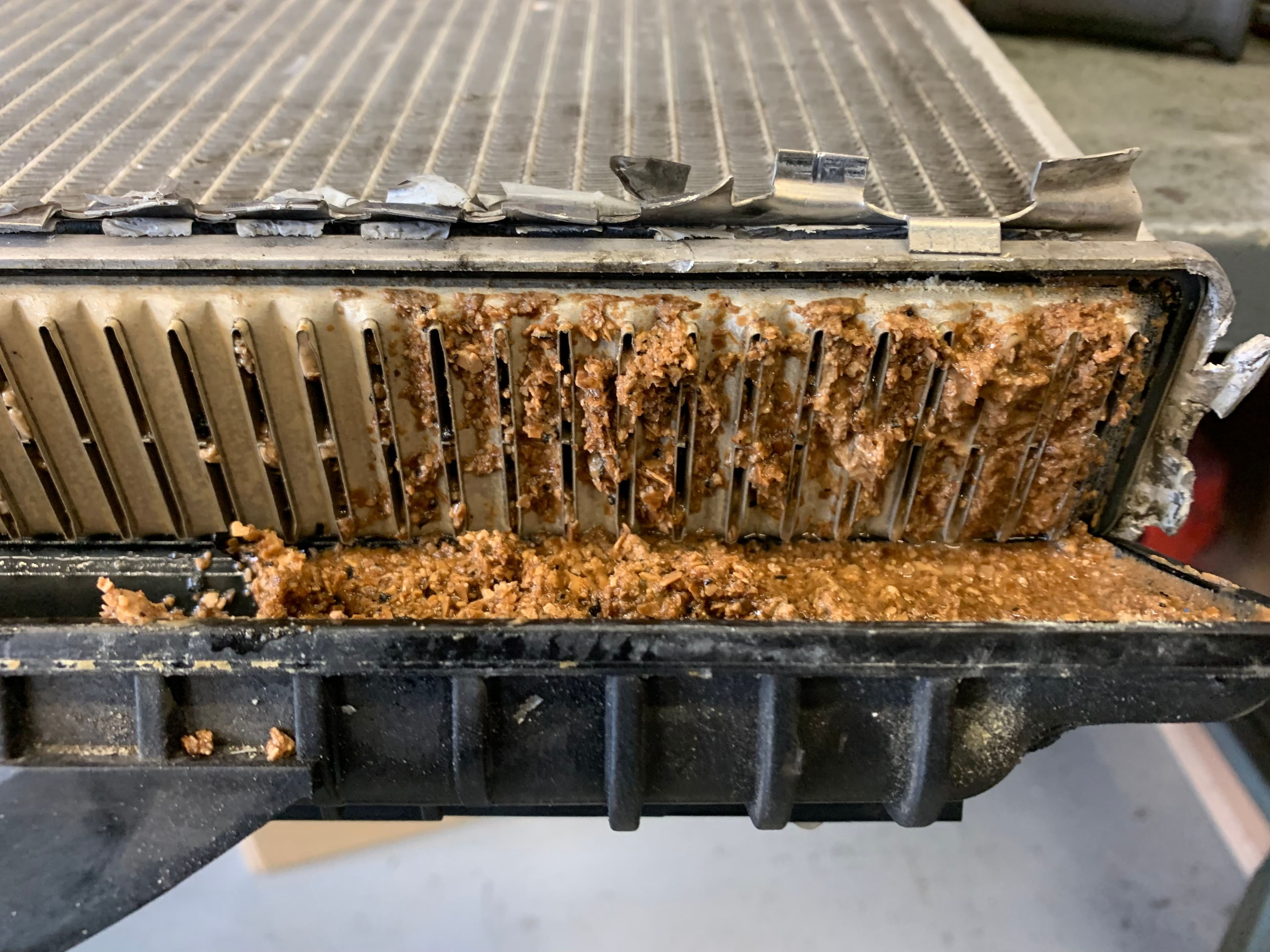 Close-up of a damaged engine coolant radiator showing severe internal corrosion and sludge buildup caused by electrolysis, with brown deposits clogging the cooling fins.