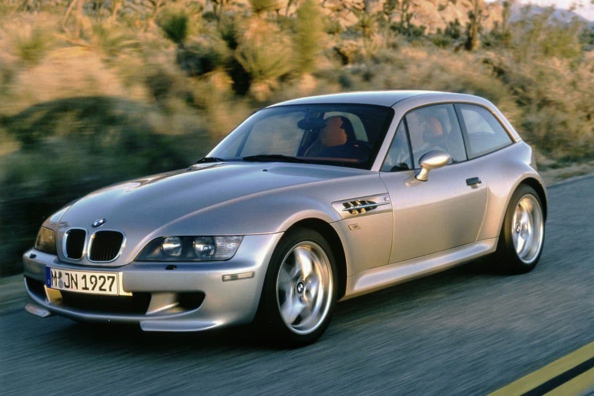 Silver BMW Z3 M Coupé driving through a desert highway at speed, showcasing its flared wheel arches and distinctive shooting brake design.