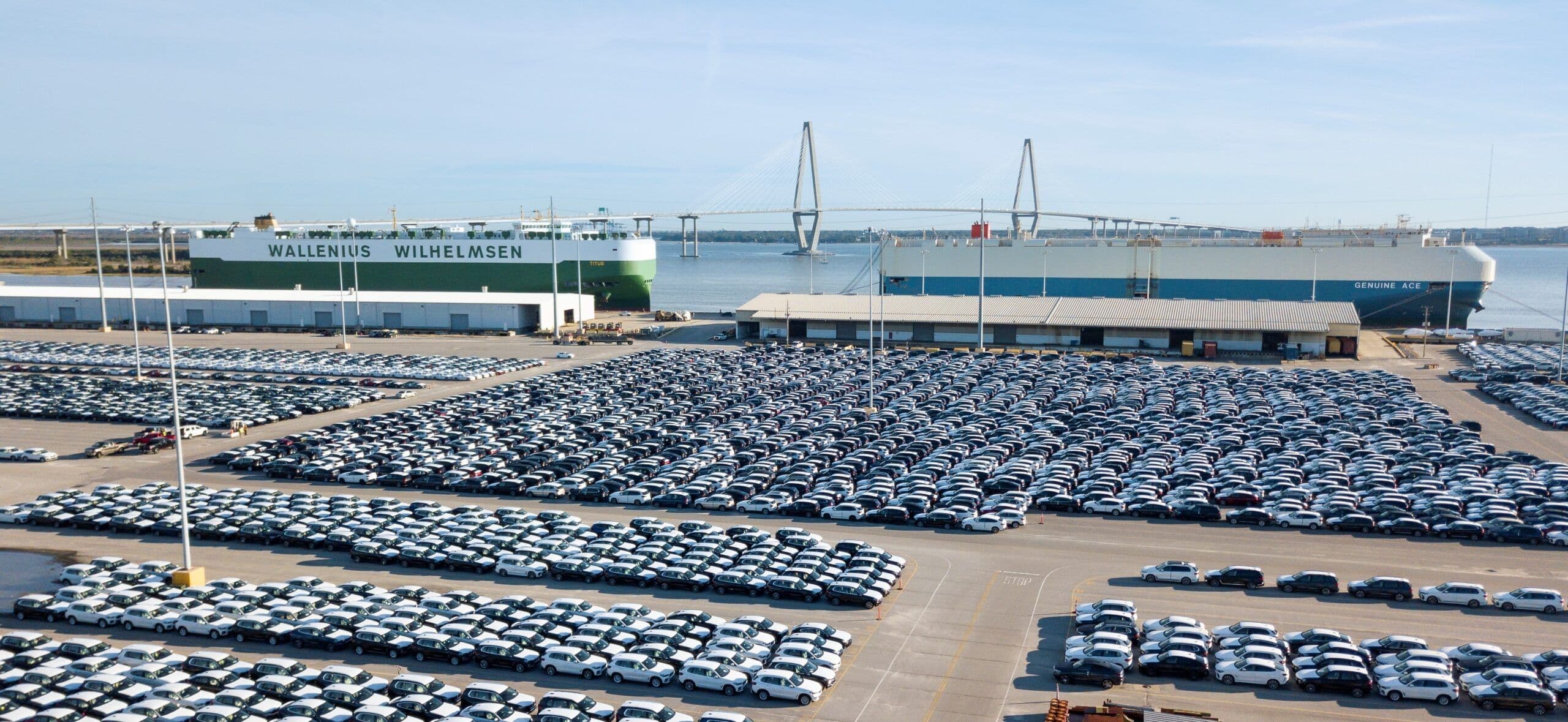 Shipping port with thousands of new cars ready for export and large cargo ships docked nearby