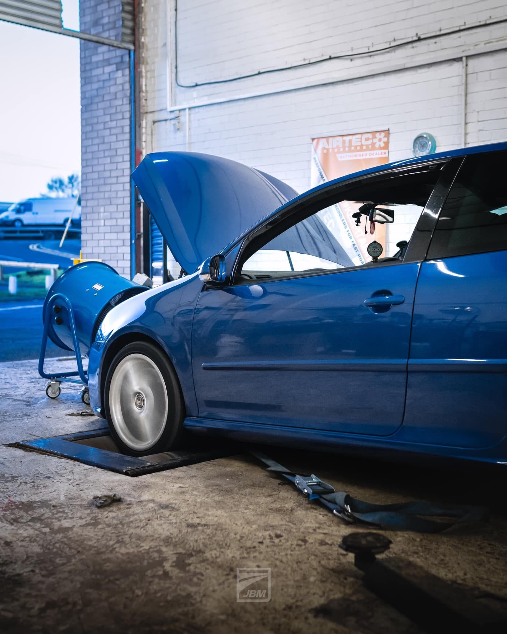 Volkswagen Golf R32 being dyno tested inside JBM Performance tuning shop, with bonnet open and wheels spinning on the rolling road.