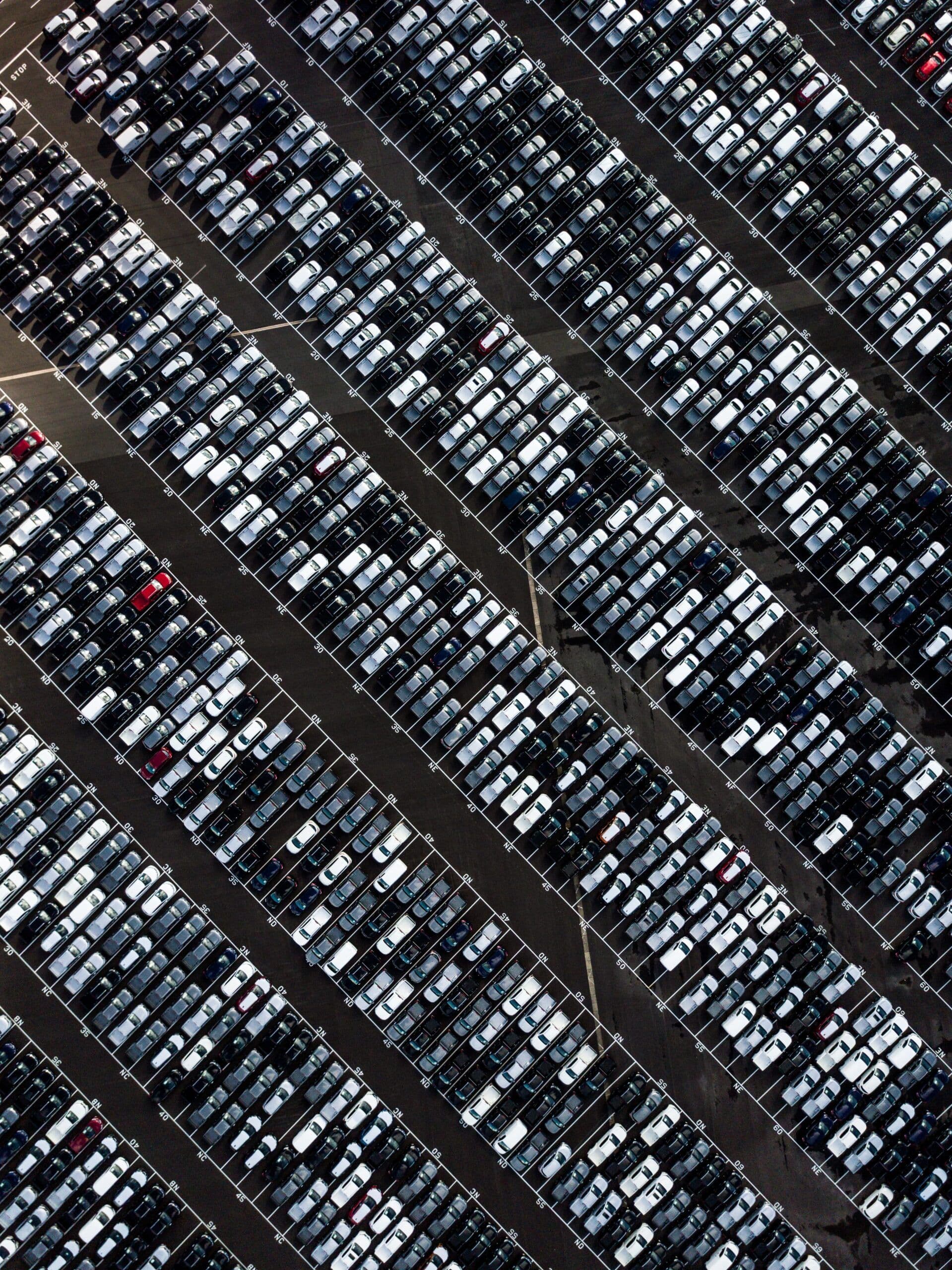 High-angle aerial view of hundreds of parked cars arranged in perfect rows at a vehicle storage or distribution facility.