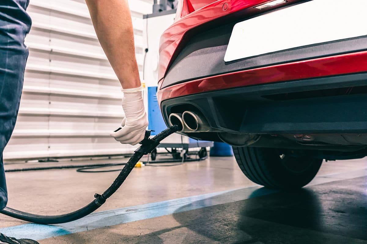 Technician inserting an exhaust probe into a car’s tailpipe during an emissions test at a workshop.