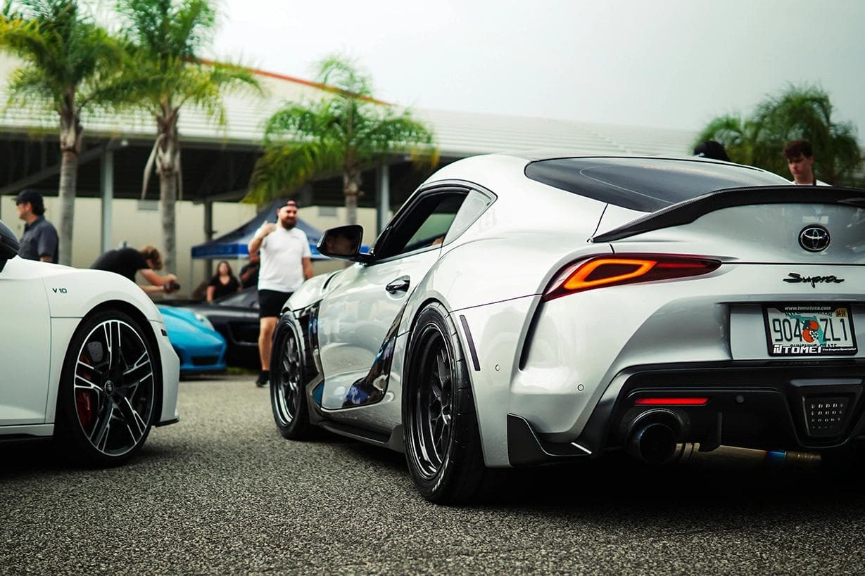 A90 Toyota GR Supra Mk5 parked at a car meet, showing its wide rear stance, performance wheels and exhaust setup.