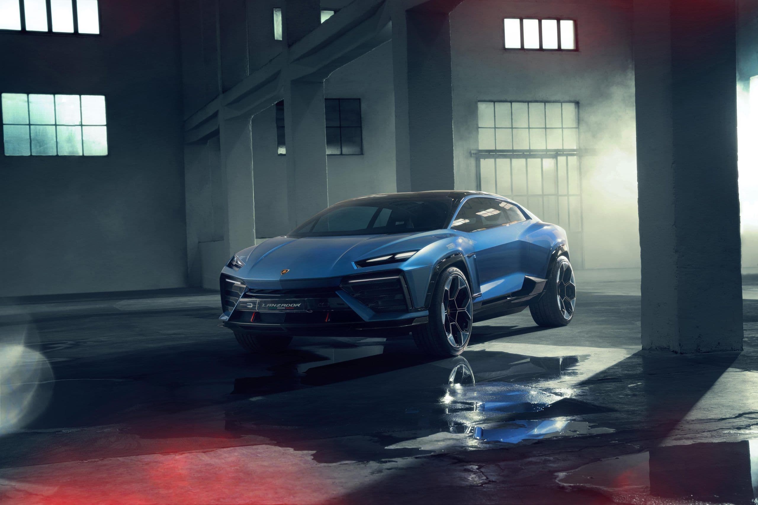 The Lamborghini Lanzador, a futuristic electric concept car in vibrant blue, showcased in a dimly lit industrial warehouse with dramatic lighting and reflective wet flooring.