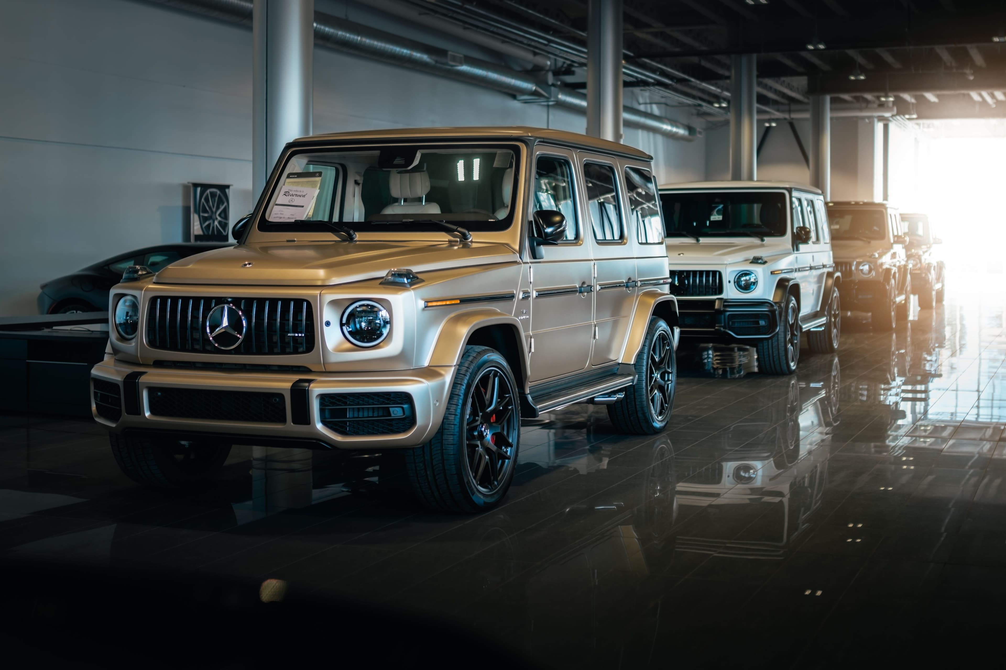Lineup of Mercedes-Benz G63 AMG SUVs inside a dealership, including a matte gold example in the foreground.