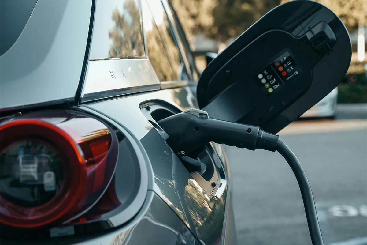 Electric vehicle plugged into a charging cable with the charge port open, showing status indicators during charging.