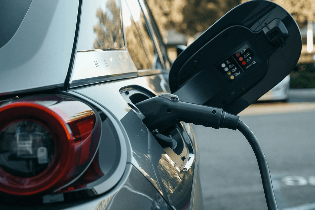Electric vehicle plugged into a charging cable with the charge port open, showing status indicators during charging.