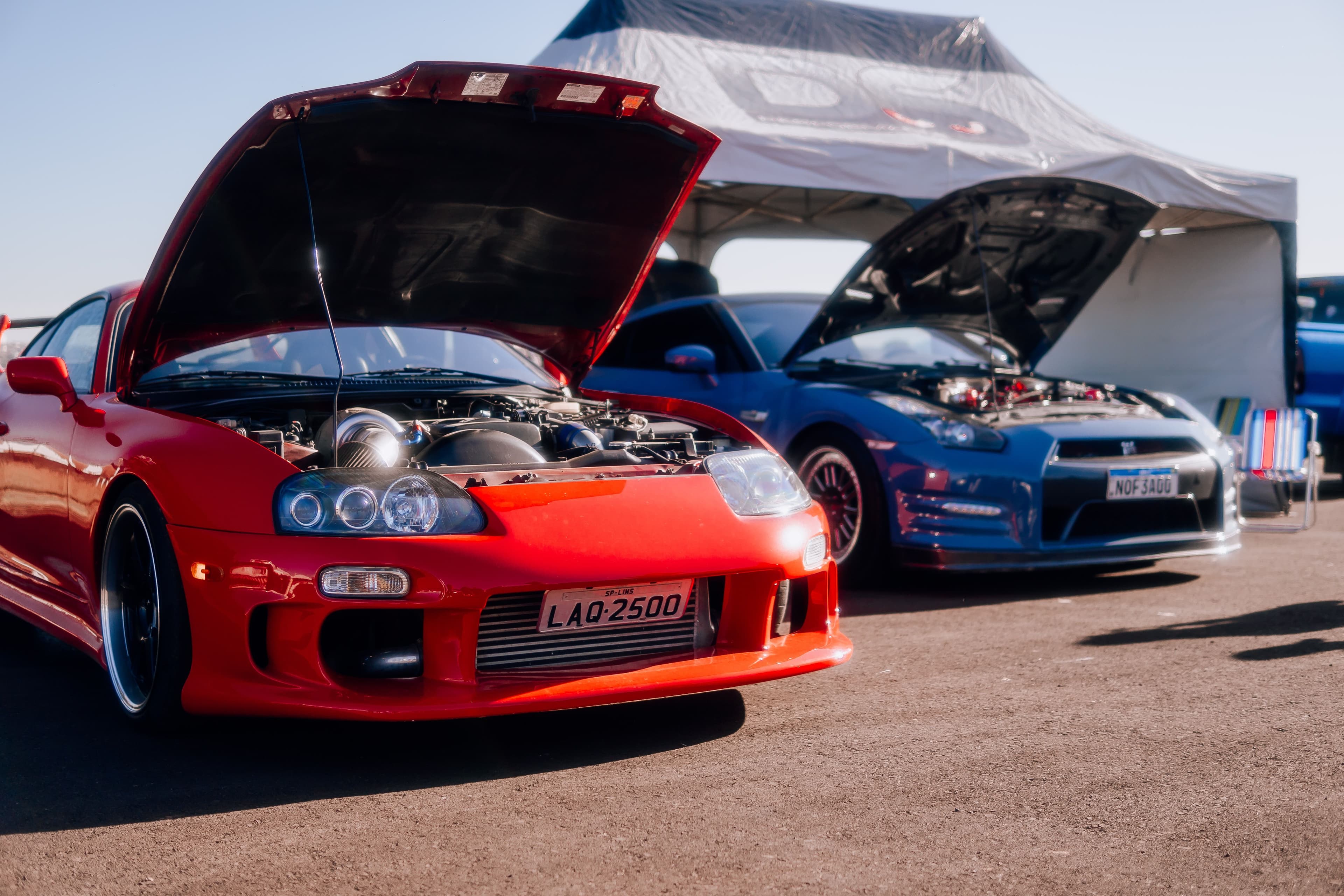 Red Toyota Supra Mk4 with twin turbos next to a Nissan GT-R R35 at a car show.