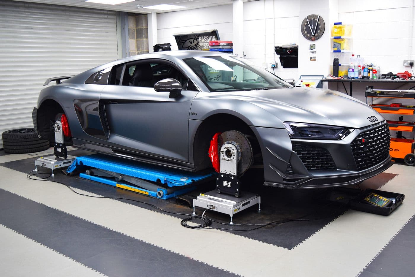 Audi R8 V10 undergoing corner weight balancing at Carbonwurks, with BG corner weight scales under each hub, red brake calipers exposed and blue scissor lift visible beneath the car