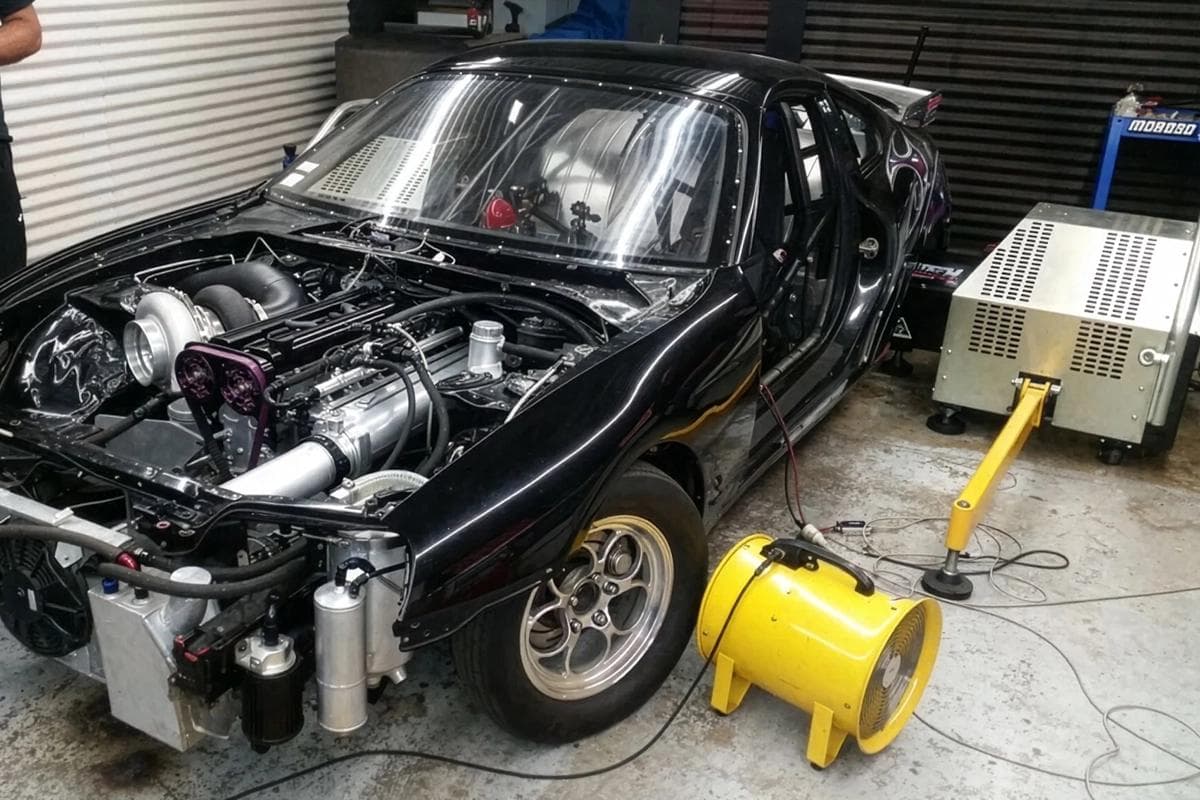 Toyota Supra Mk4 with a 2JZ engine mounted on a hub dyno with the wheels removed and cooling fans placed at the front during a power run.