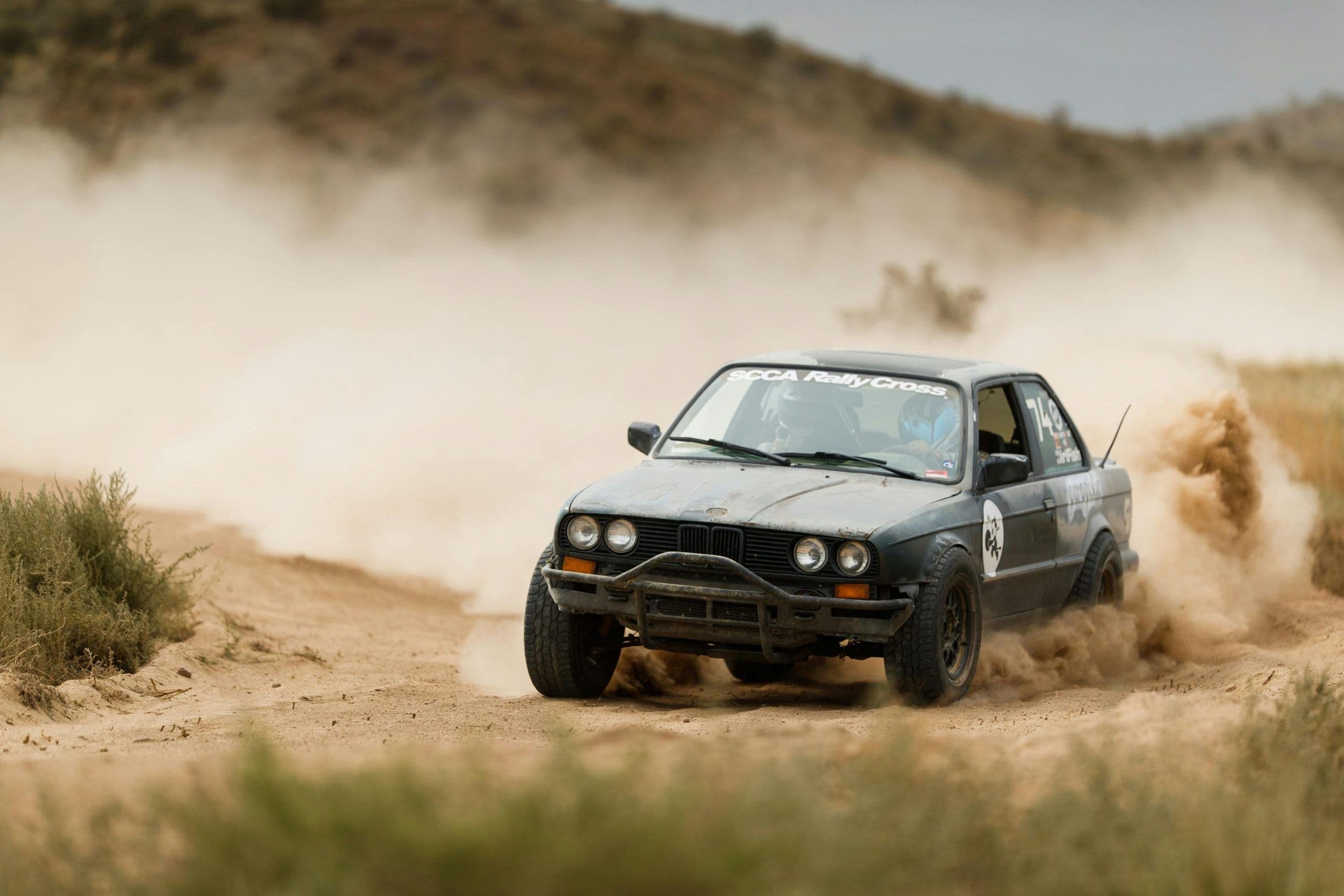 BMW E30 rally car kicking up dust during an SCCA RallyCross stage in the desert.