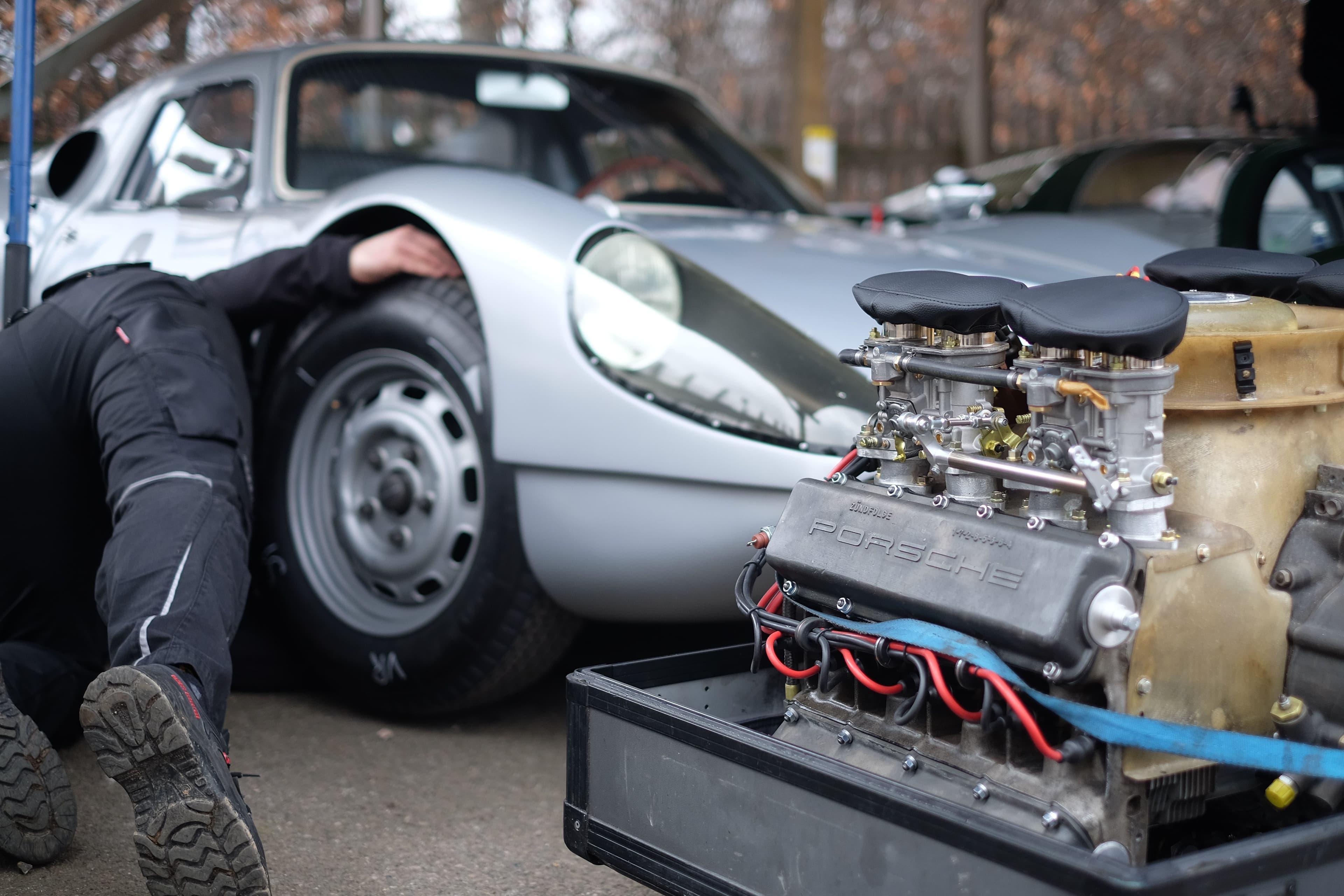 Mechanic working on a vintage Porsche race car with a detached flat-six engine.