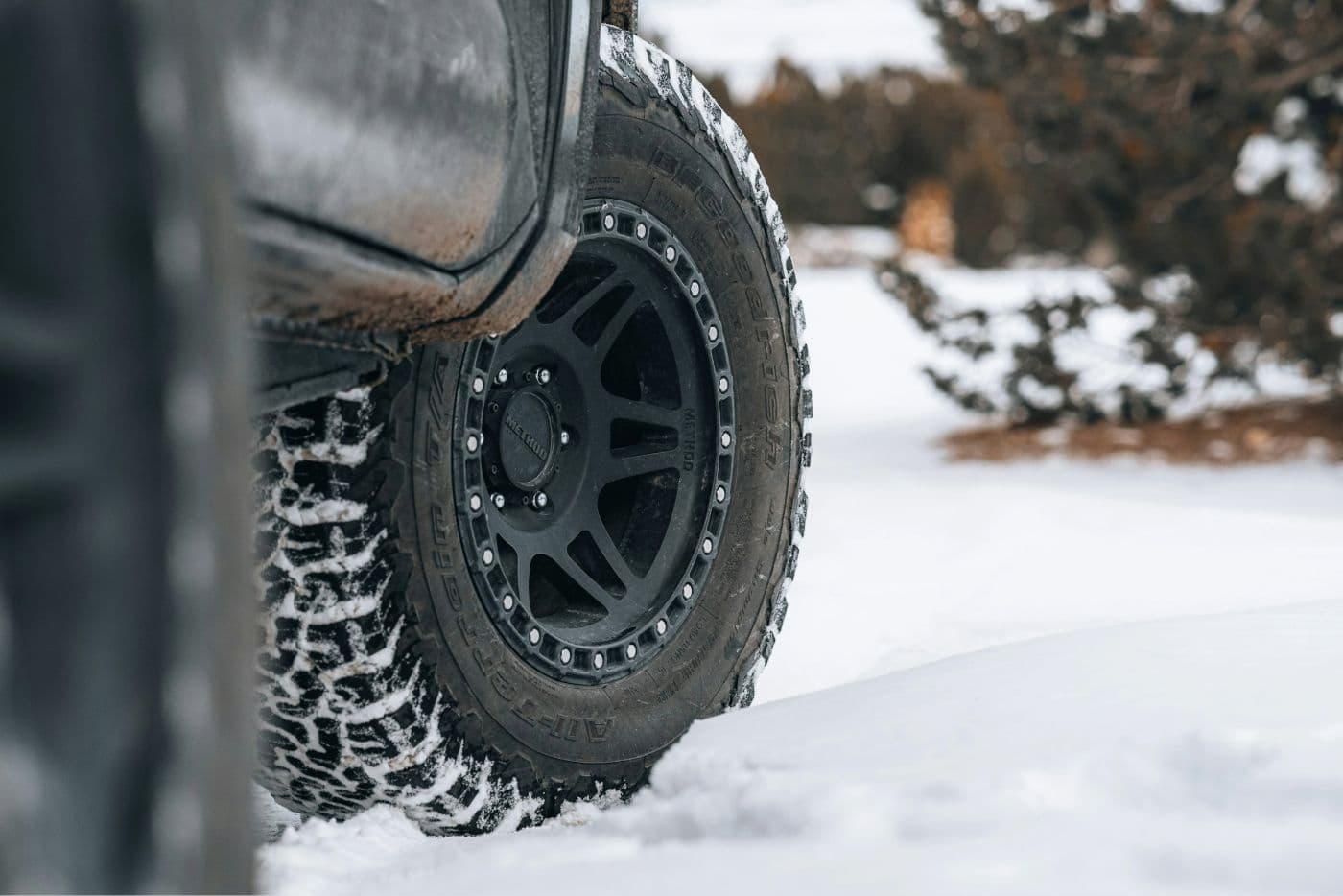 Close-up of an all-terrain tyre on an off-road truck driving through snow-covered terrain