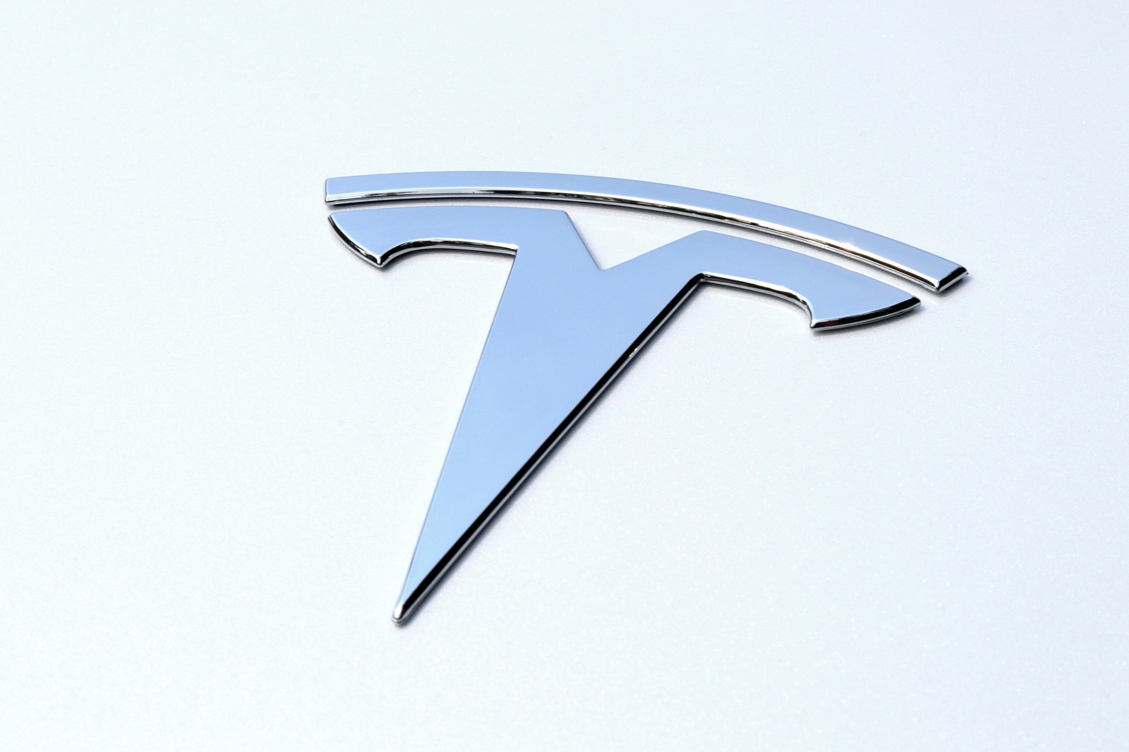 A close-up of a chrome Tesla emblem on a glossy white car body.