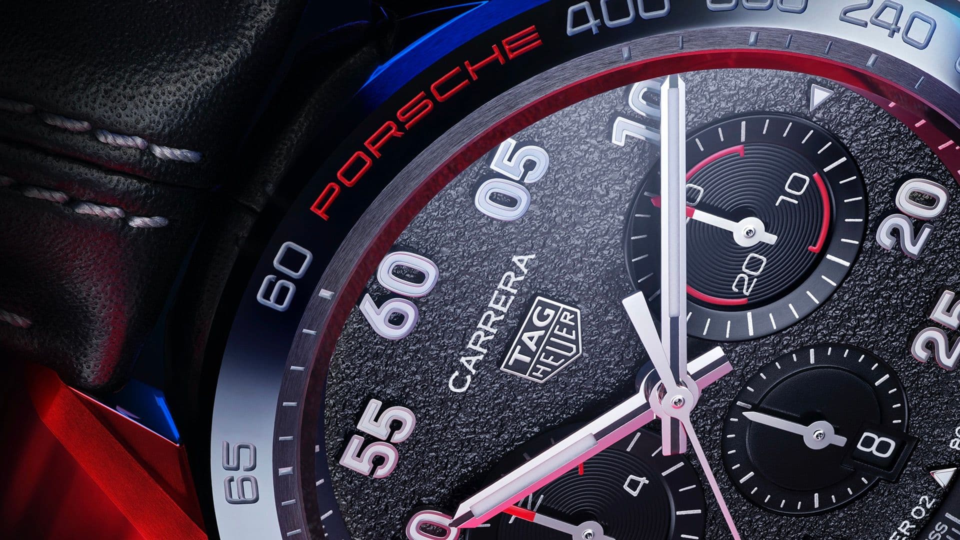 Macro shot of a TAG Heuer Carrera Porsche chronograph watch dial, highlighting the textured face, sub-dials, and red PORSCHE branding on the bezel.