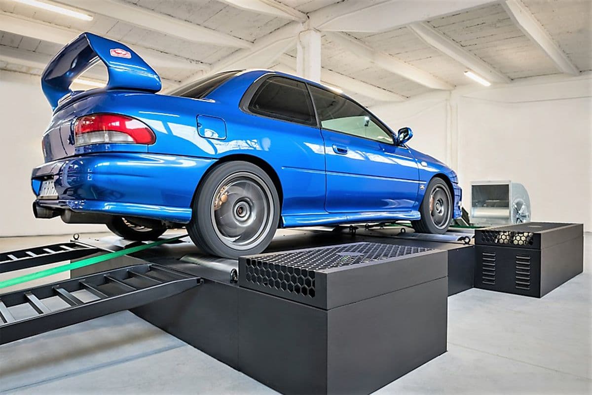 Blue Subaru Impreza GC8 running on a dynamometer during performance testing inside a workshop.