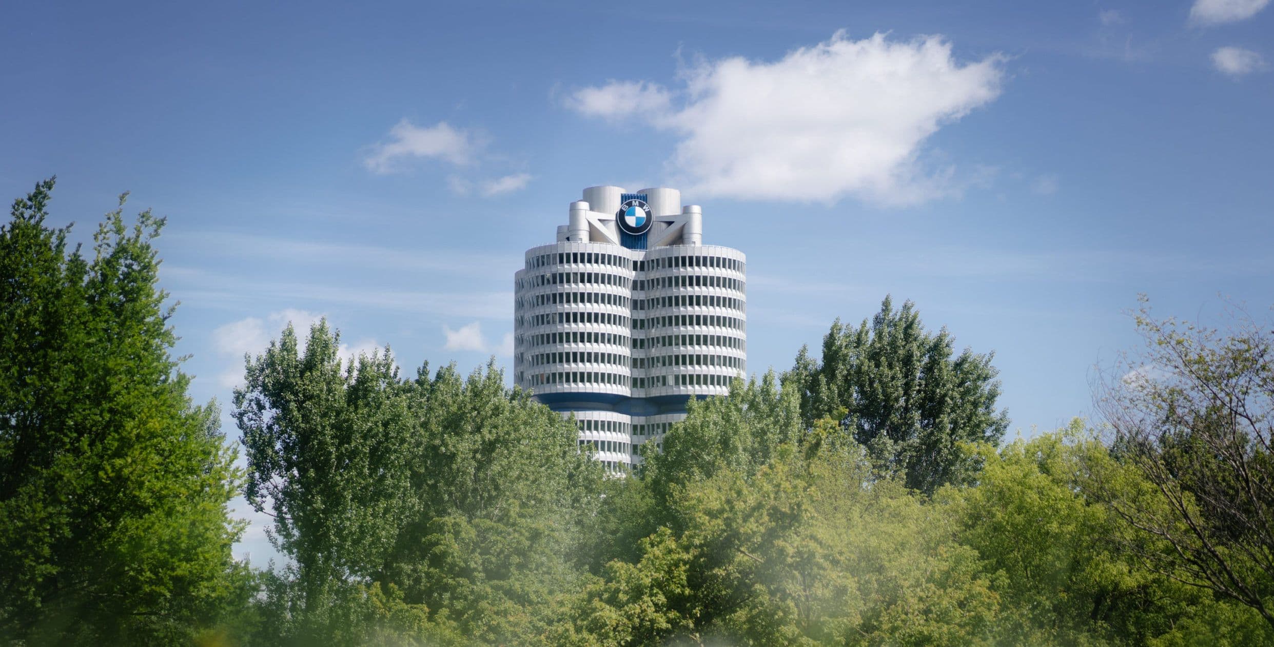 BMW headquarters in Munich, Germany, featuring the iconic four-cylinder tower above green trees