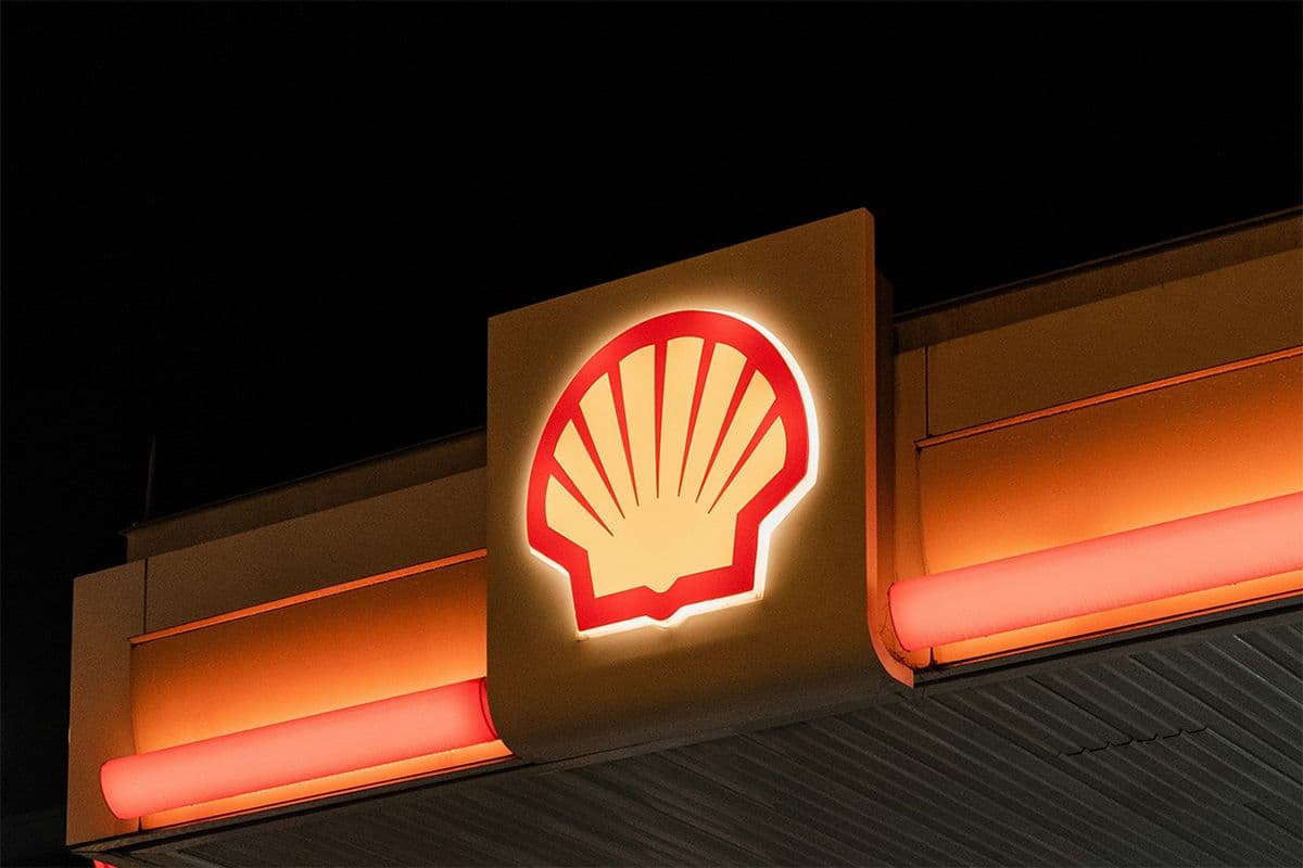 Illuminated Shell petrol station sign glowing at night against a black sky, highlighting the brand’s presence in fuel retail.
