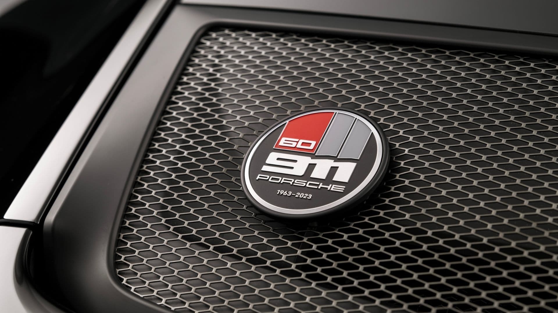 Close-up of Porsche 911 60th Anniversary badge on mesh engine cover, celebrating 1963–2023.
