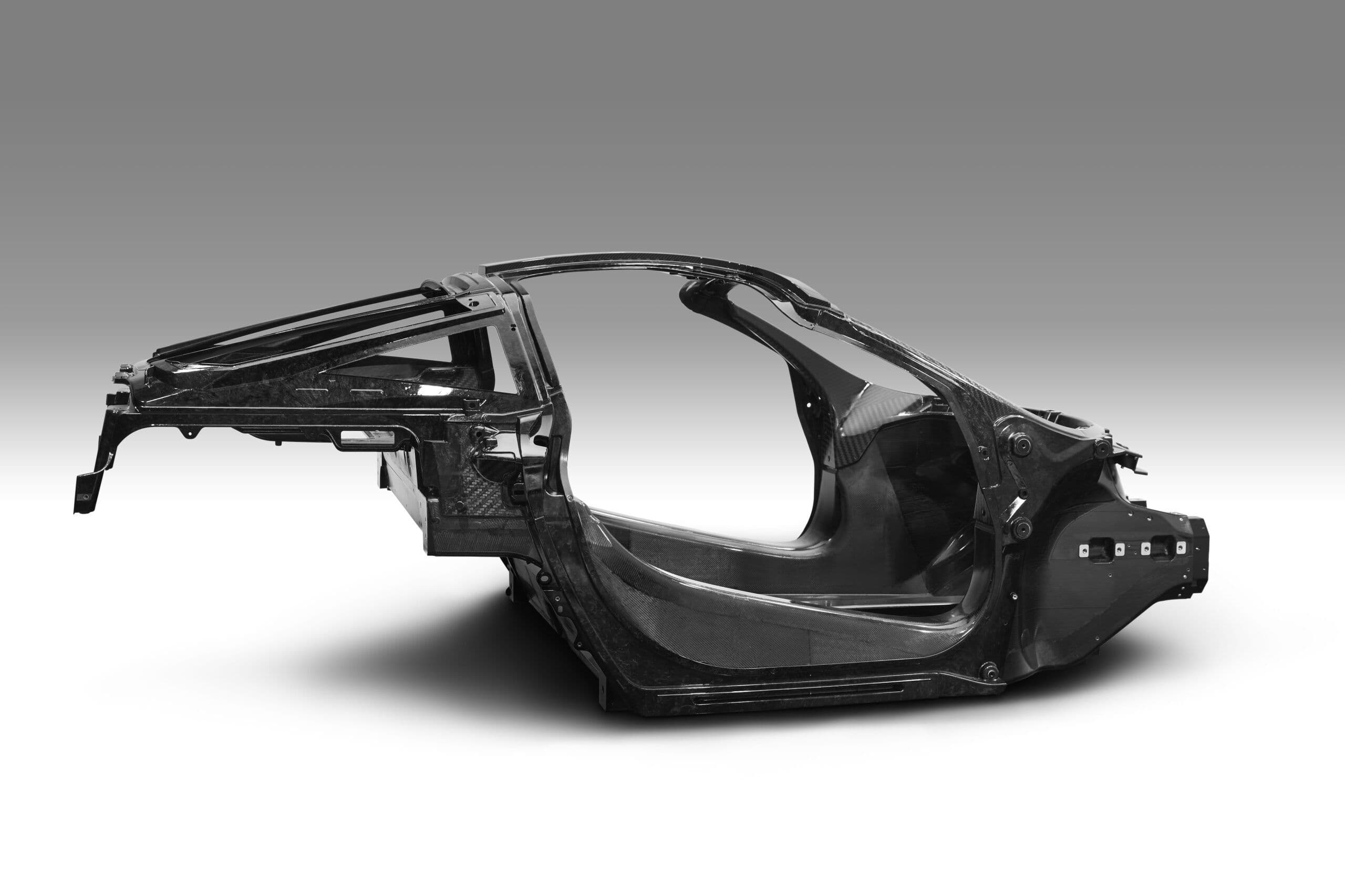 A side view of a McLaren Monocage II carbon fibre monocoque chassis, isolated on a gradient grey background, showcasing the structural tub used in McLaren’s road cars.