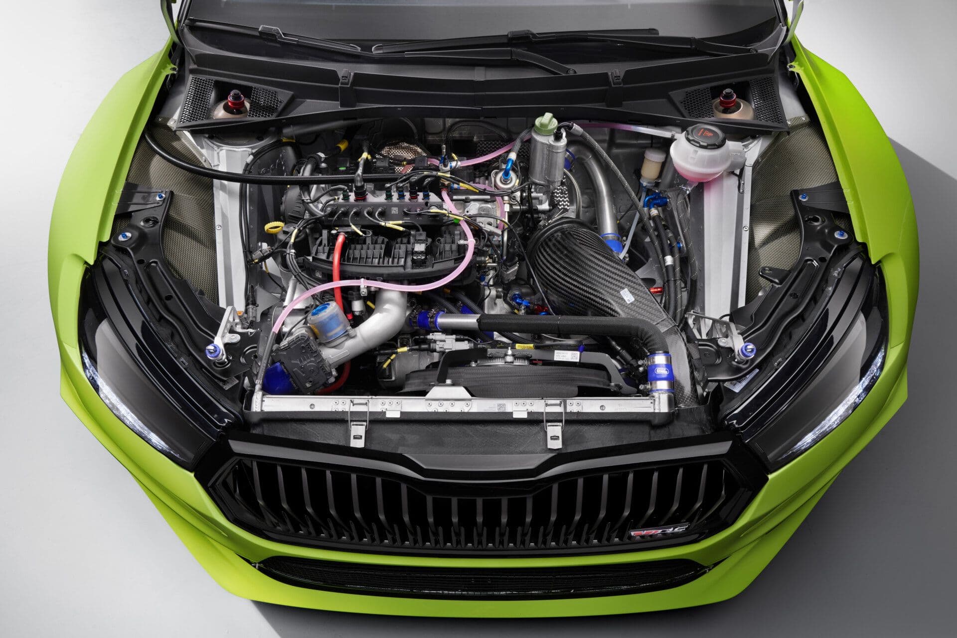 Close-up view of the engine bay of the Škoda Fabia RS Rally2 race car, showcasing its high-performance turbocharged powertrain, intricate wiring, carbon fibre intake system, and motorsport-spec components, all housed within a vivid green front end.