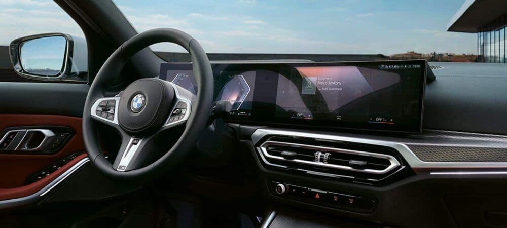 Interior of a modern BMW featuring a curved widescreen digital display, sporty steering wheel, and minimalist dashboard design.