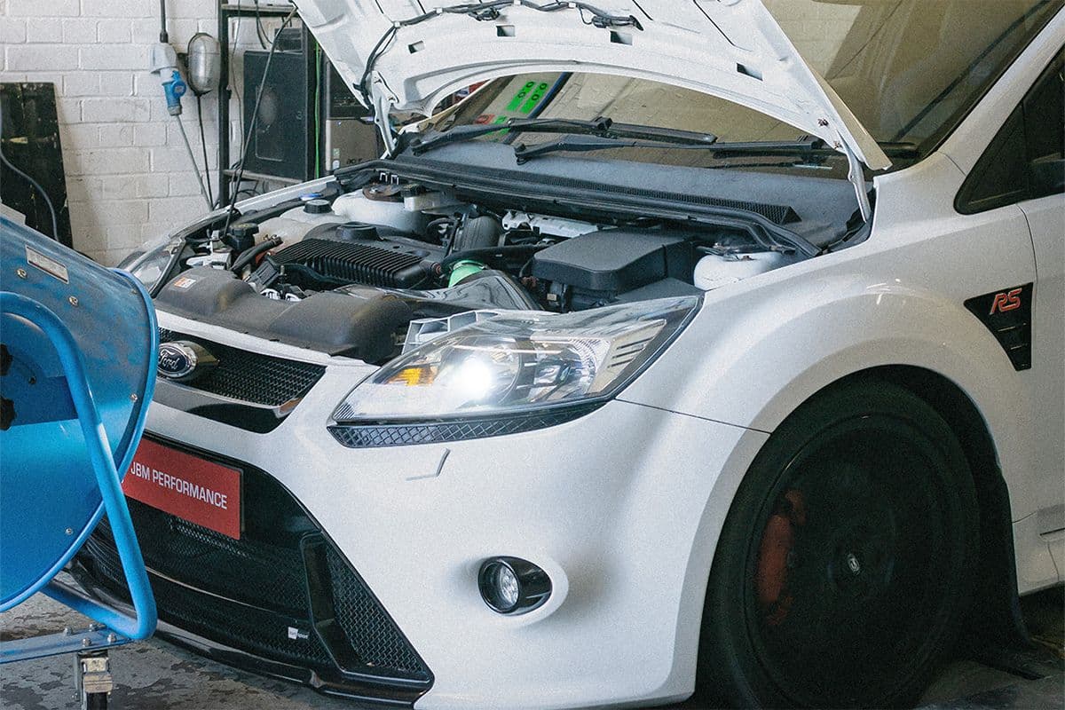 White Ford Focus RS on a dyno at JBM Performance with the bonnet open during an engine tuning session.