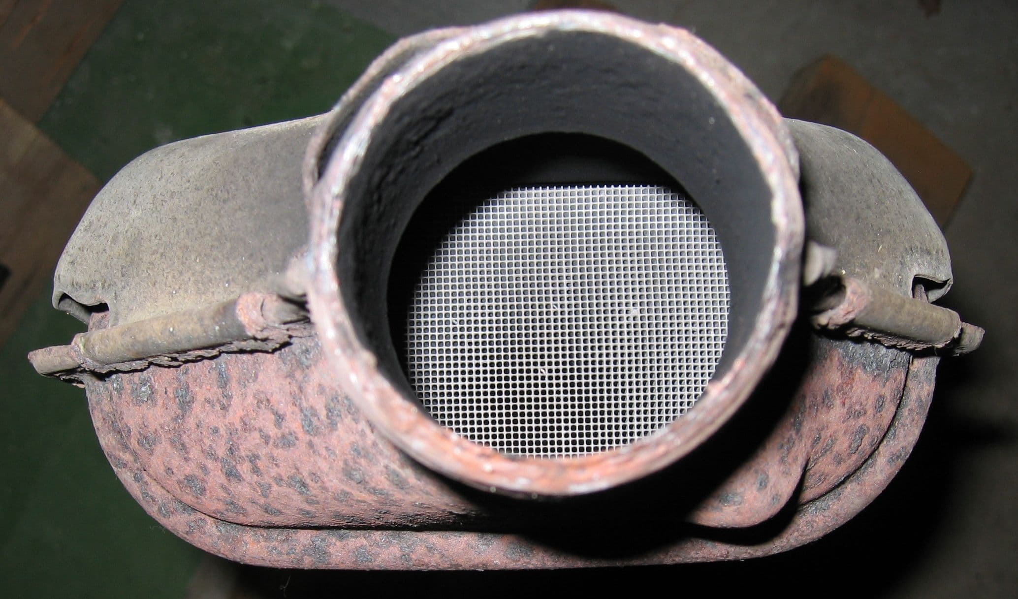 Close up of a catalytic converter showing the ceramic honeycomb monolith inside a used metal housing.