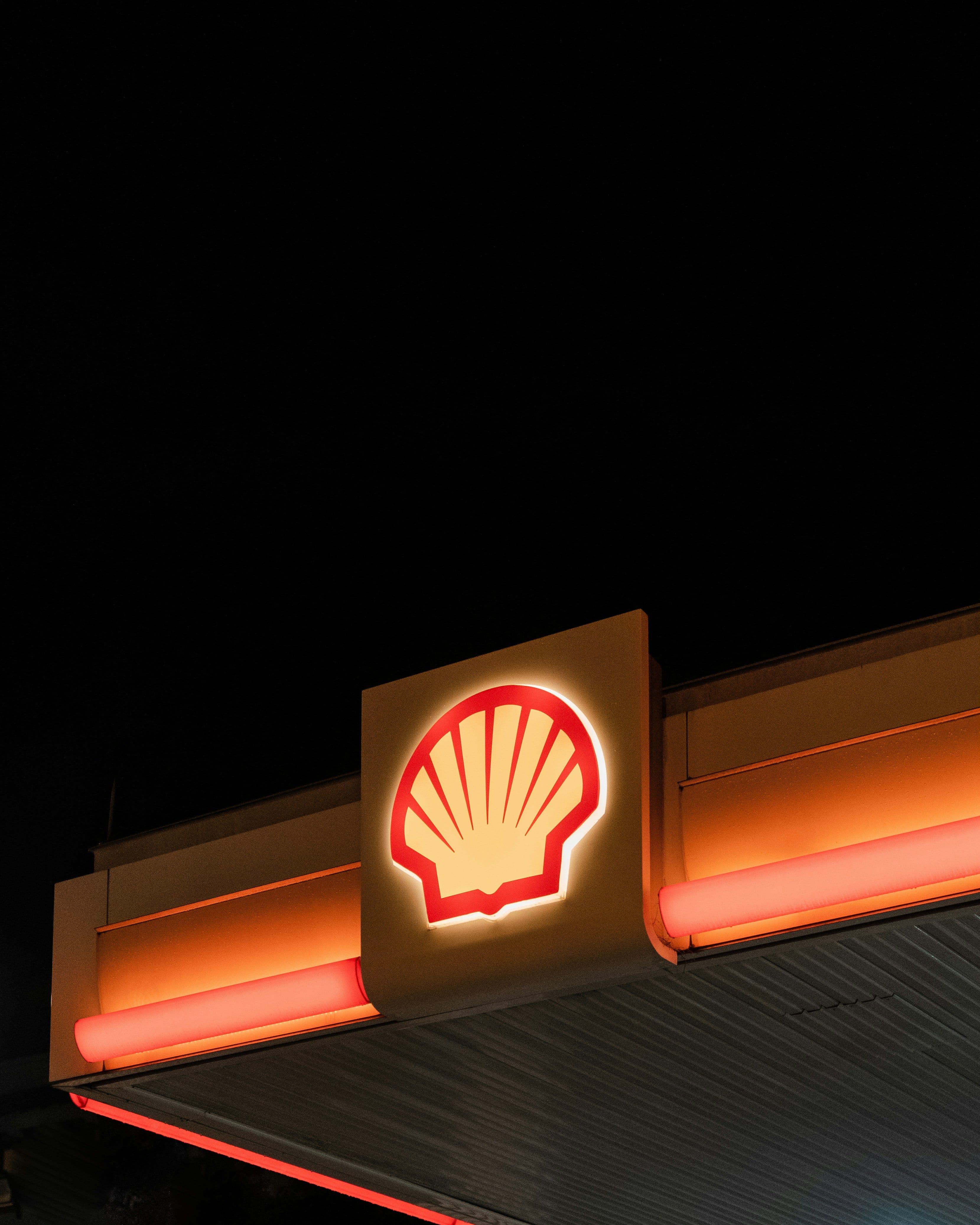 Illuminated Shell petrol station sign glowing at night against a black sky, highlighting the brand’s presence in fuel retail.