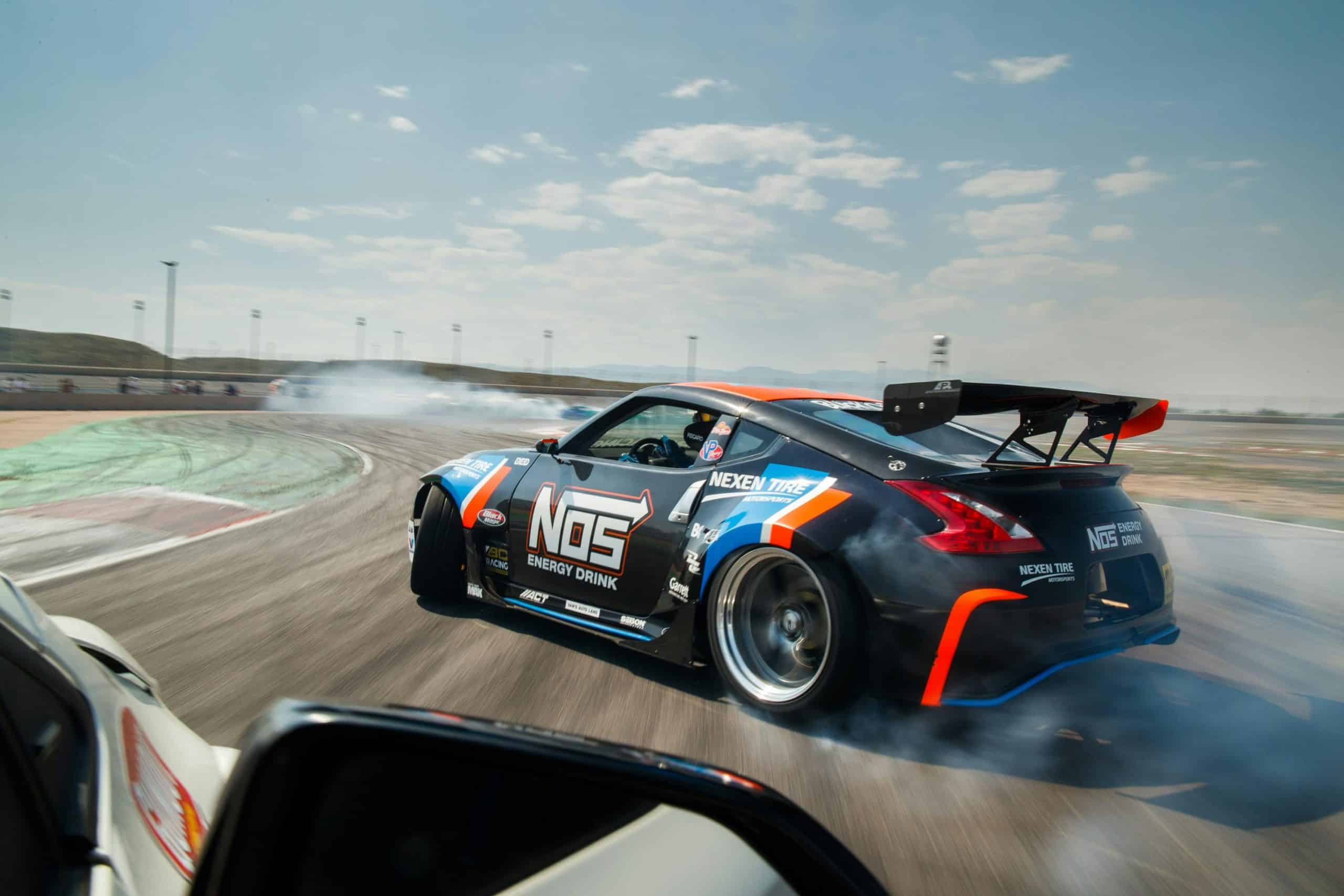 Chris Forsberg drifting his NOS Energy Drink Nissan 370Z during a Formula Drift event, producing tyre smoke through a high-speed corner with Nexen Tire sponsorship visible.